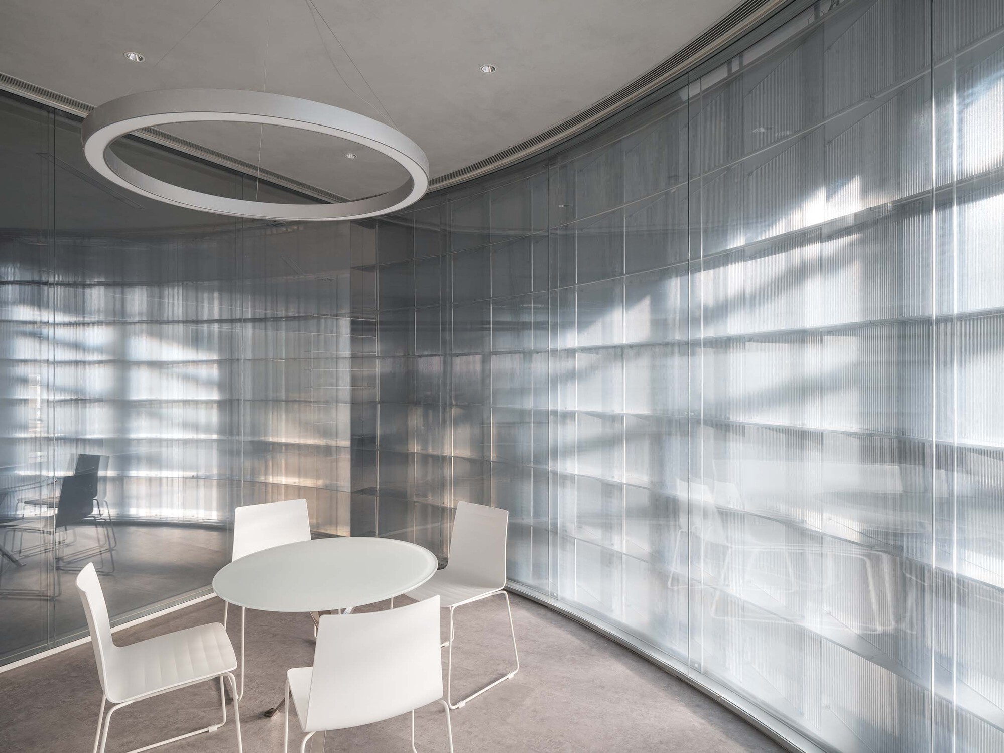 Meeting room with circular ring light fixture and translucent glass walls filtering exterior shadows