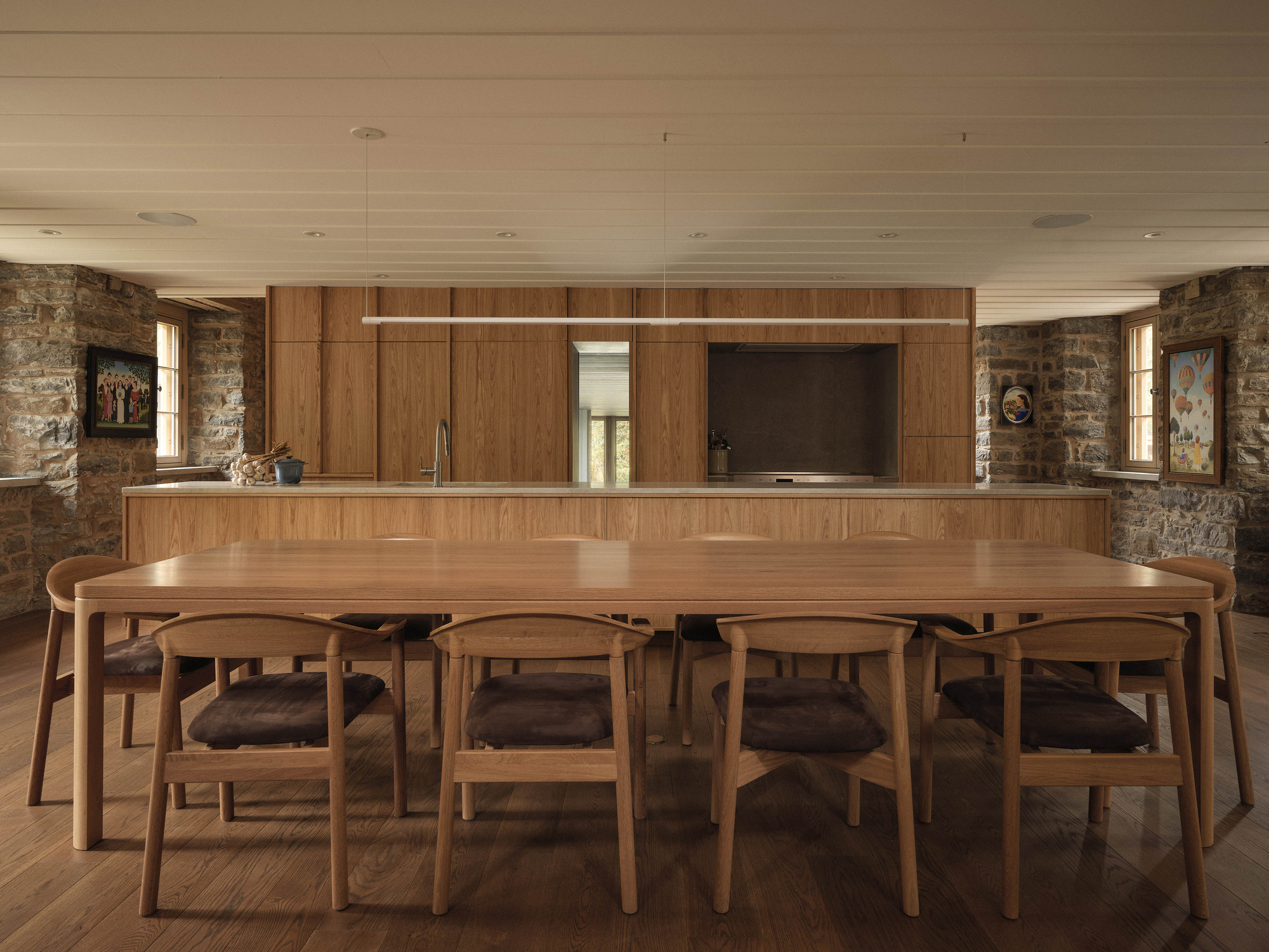 Open kitchen and dining area with timber cabinetry, pendant light, and stone walls framing narrow windows
