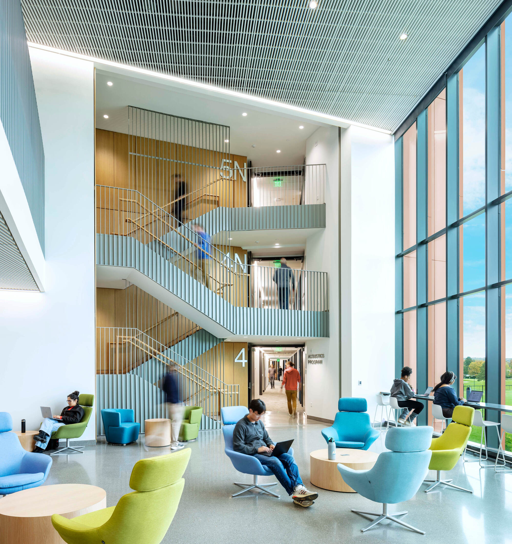 Four-story stairwell with vertical slatted walls, students on seating below, and tall glazing to one side