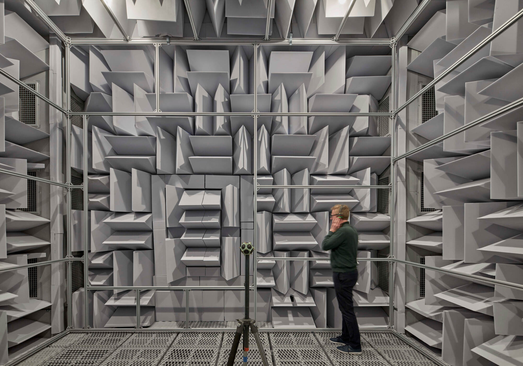 Acoustic testing chamber lined with pyramidal foam baffles and a technician adjusting equipment inside