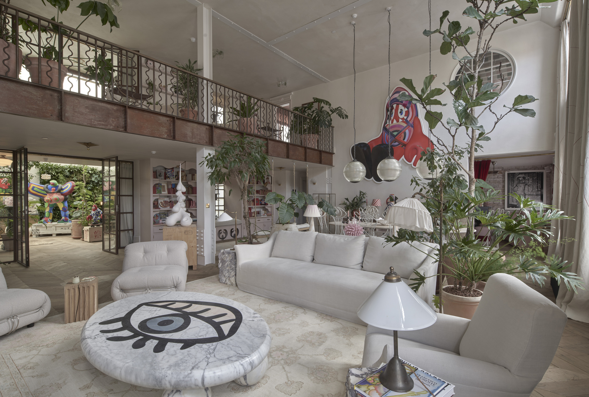 Double-height living room with metal balcony railing, indoor plants, and an eye-motif coffee table