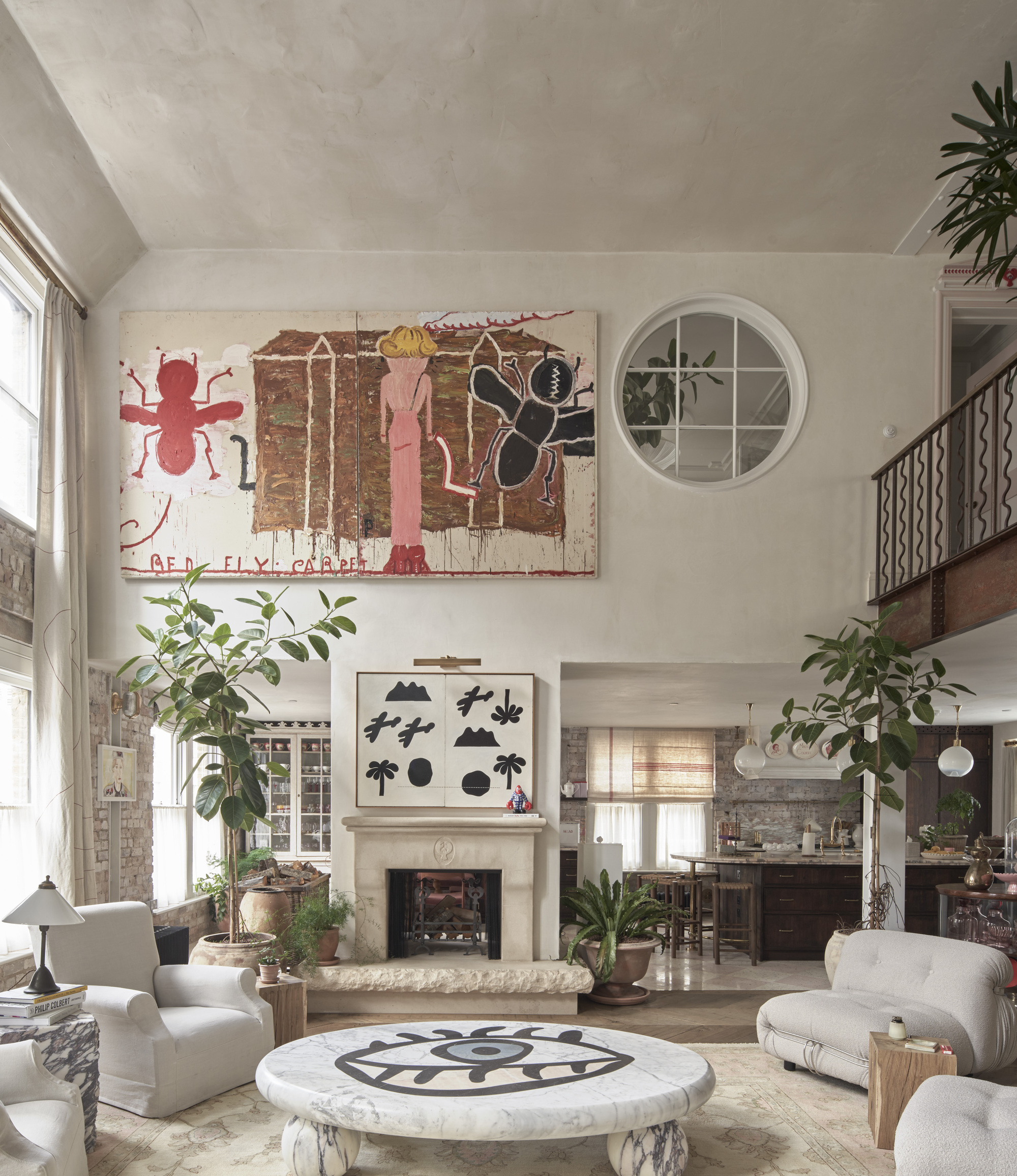 Double-height living space with exposed brick walls, round porthole window, and fireplace below graphic artwork