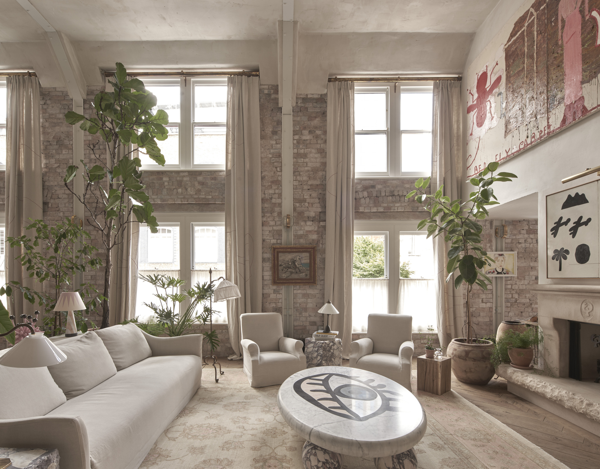 Seating area with tall windows, indoor ficus trees, exposed brick walls, and diffused daylight through linen curtains
