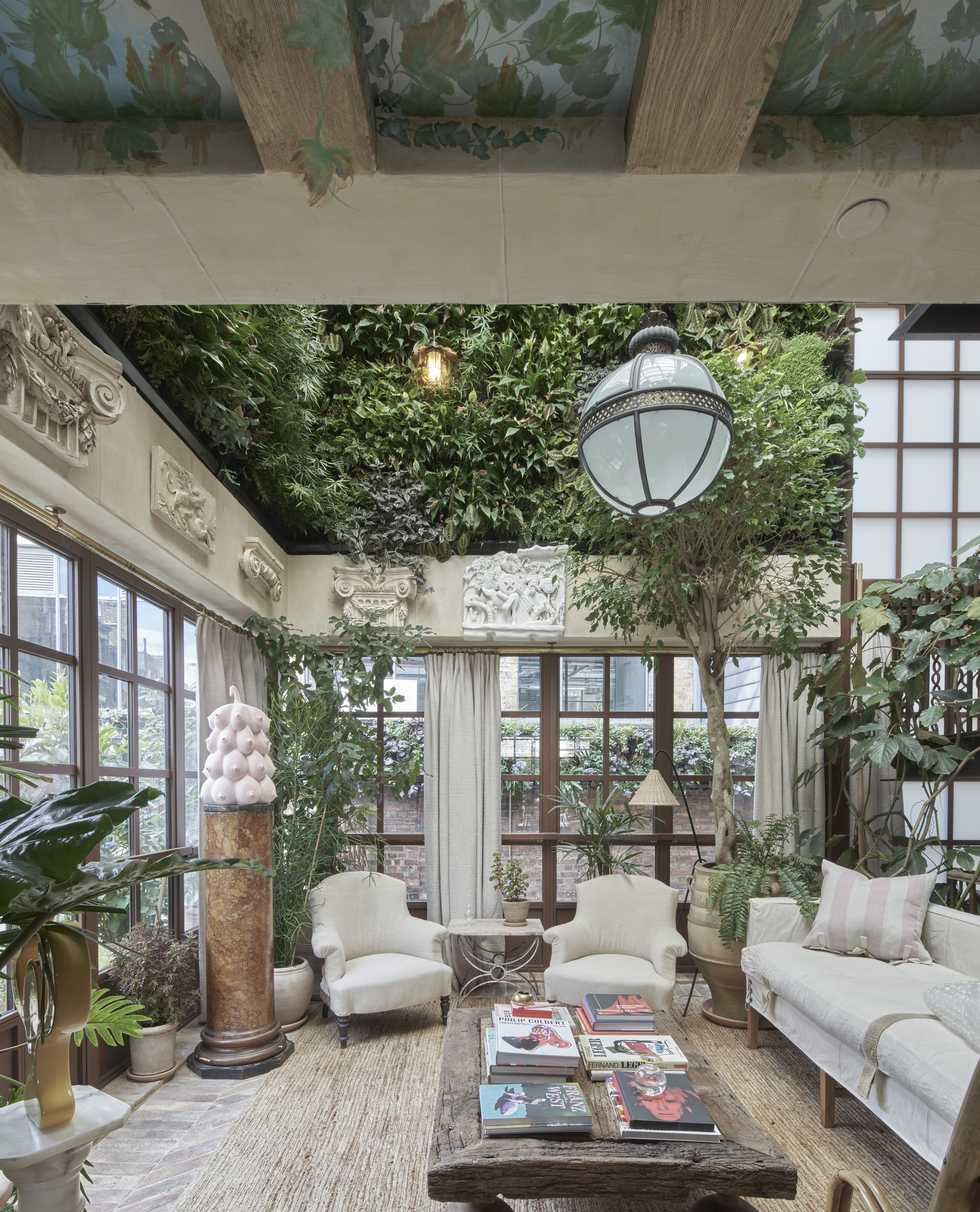 Interior conservatory with ornamental plaster moldings, gridded windows, and ceiling-mounted greenery illuminated by pendant lights