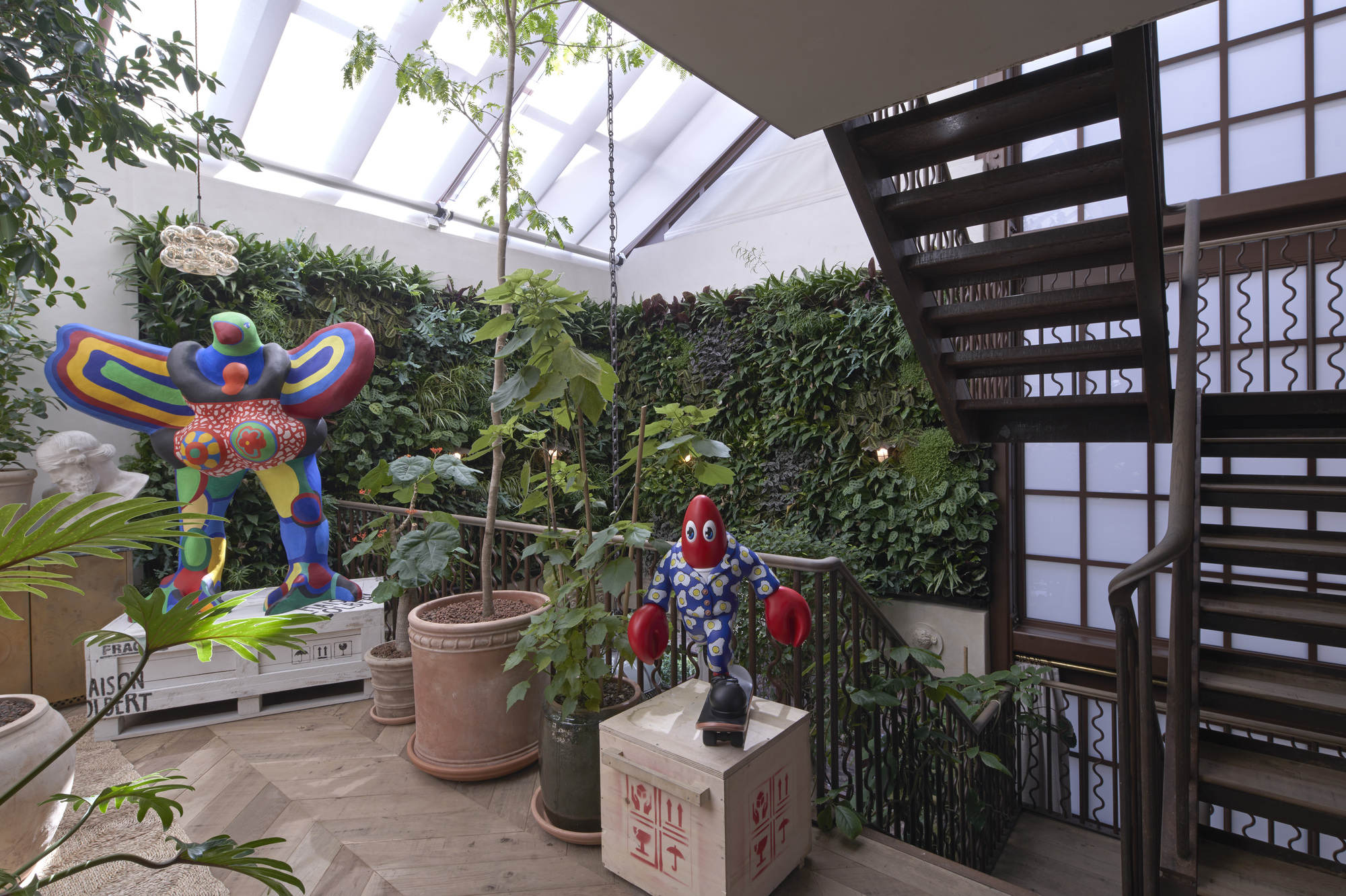 Glazed skylight atrium with vertical green wall, sculptural figures in planters, and dark timber staircase with patterned railings
