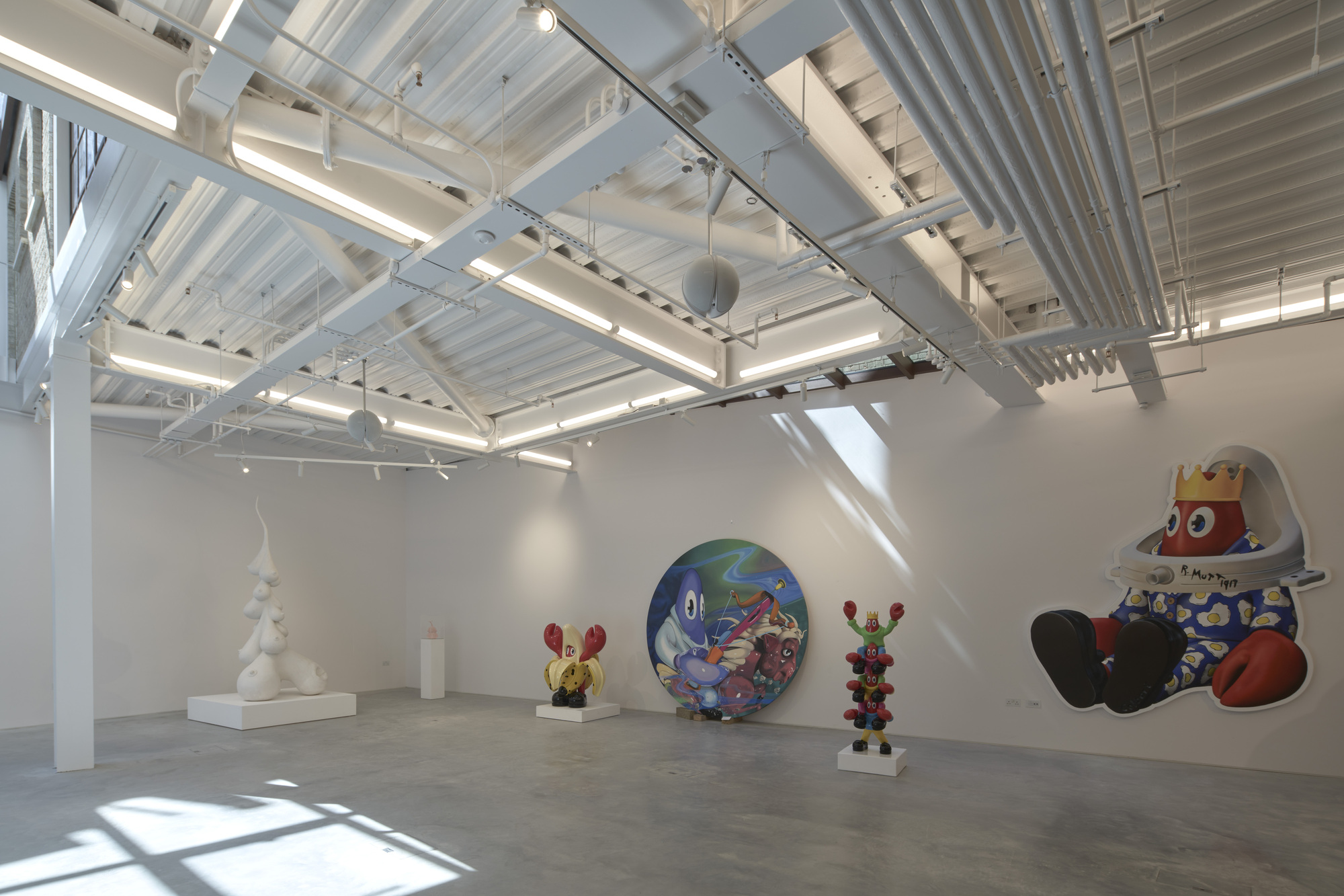 Gallery interior with exposed ceiling beams and track lighting illuminating white walls and polished concrete floor