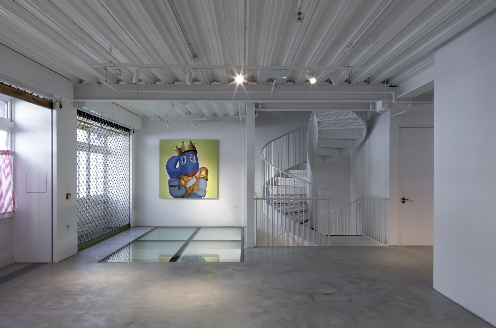 White spiral staircase behind mesh railing next to floor opening with glazed panels and pendant lights