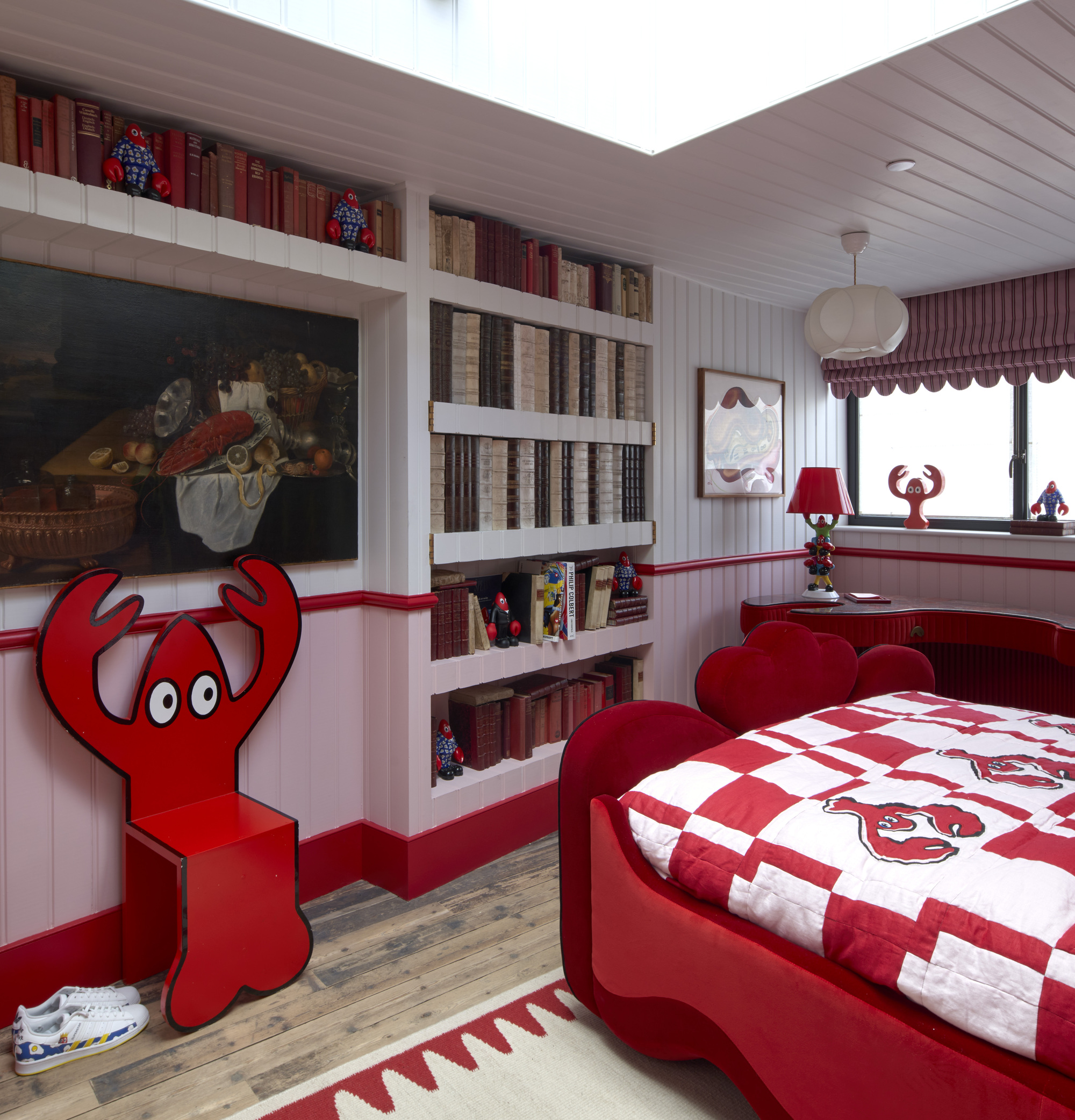 Bedroom with built-in shelving displaying books and red-themed furnishings beneath a skylight