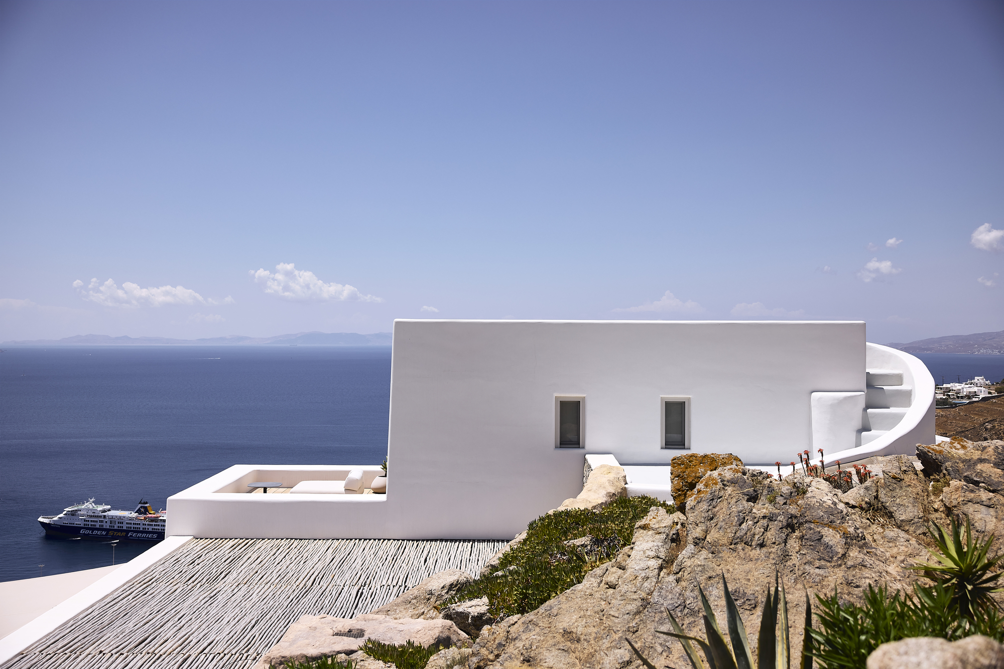 White rendered facade with curved spiral staircase and two small windows overlooking the blue sea