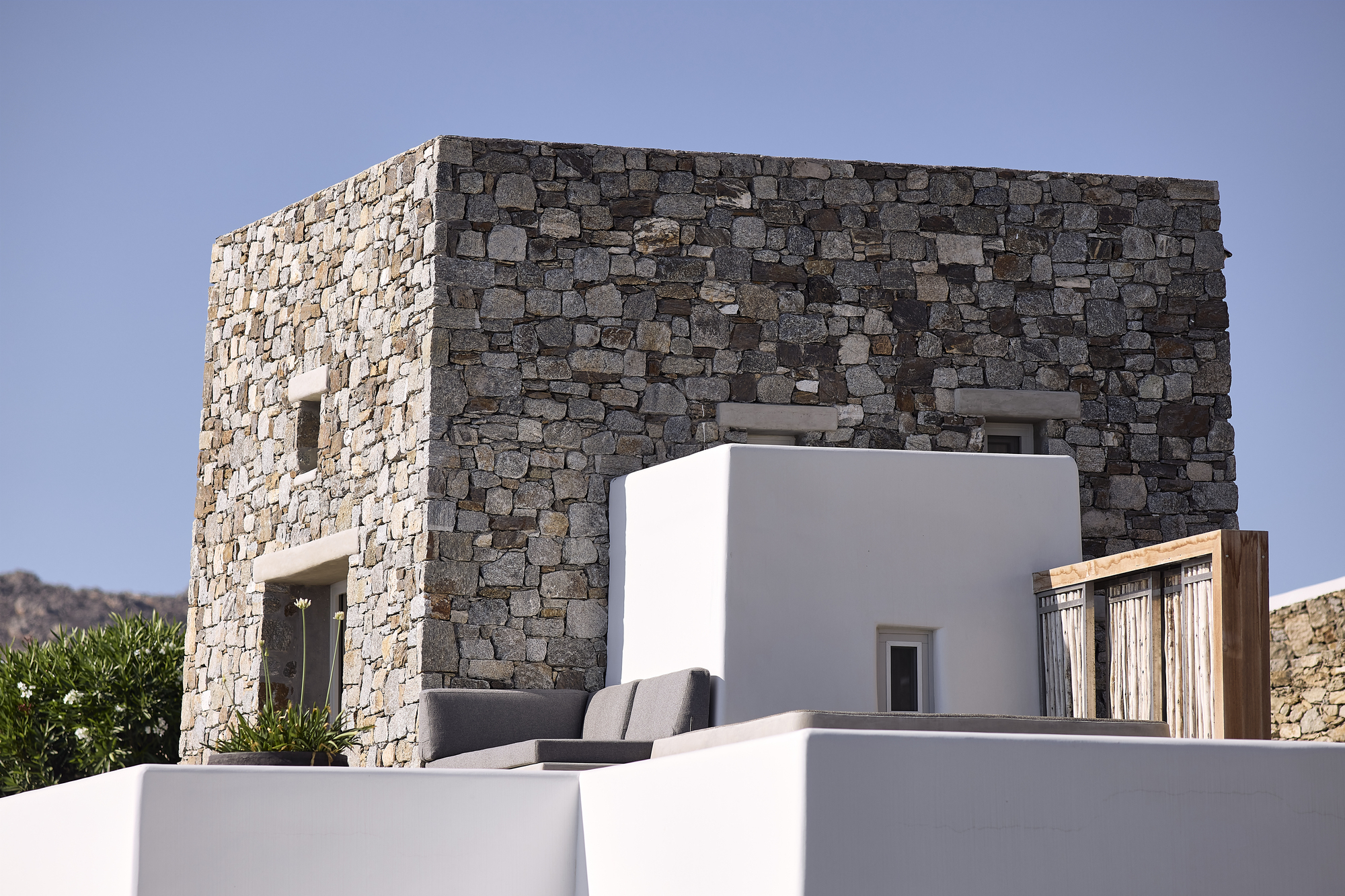 Stone masonry tower rising above white rendered volumes under a clear blue sky