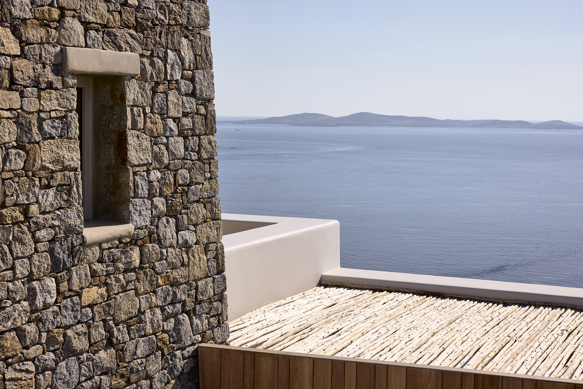 Timber roof deck with stone wall opening framing distant islands across the sea