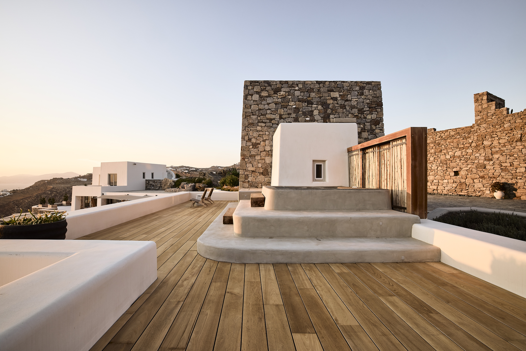 Timber deck with curved concrete steps leading to white volume at dusk
