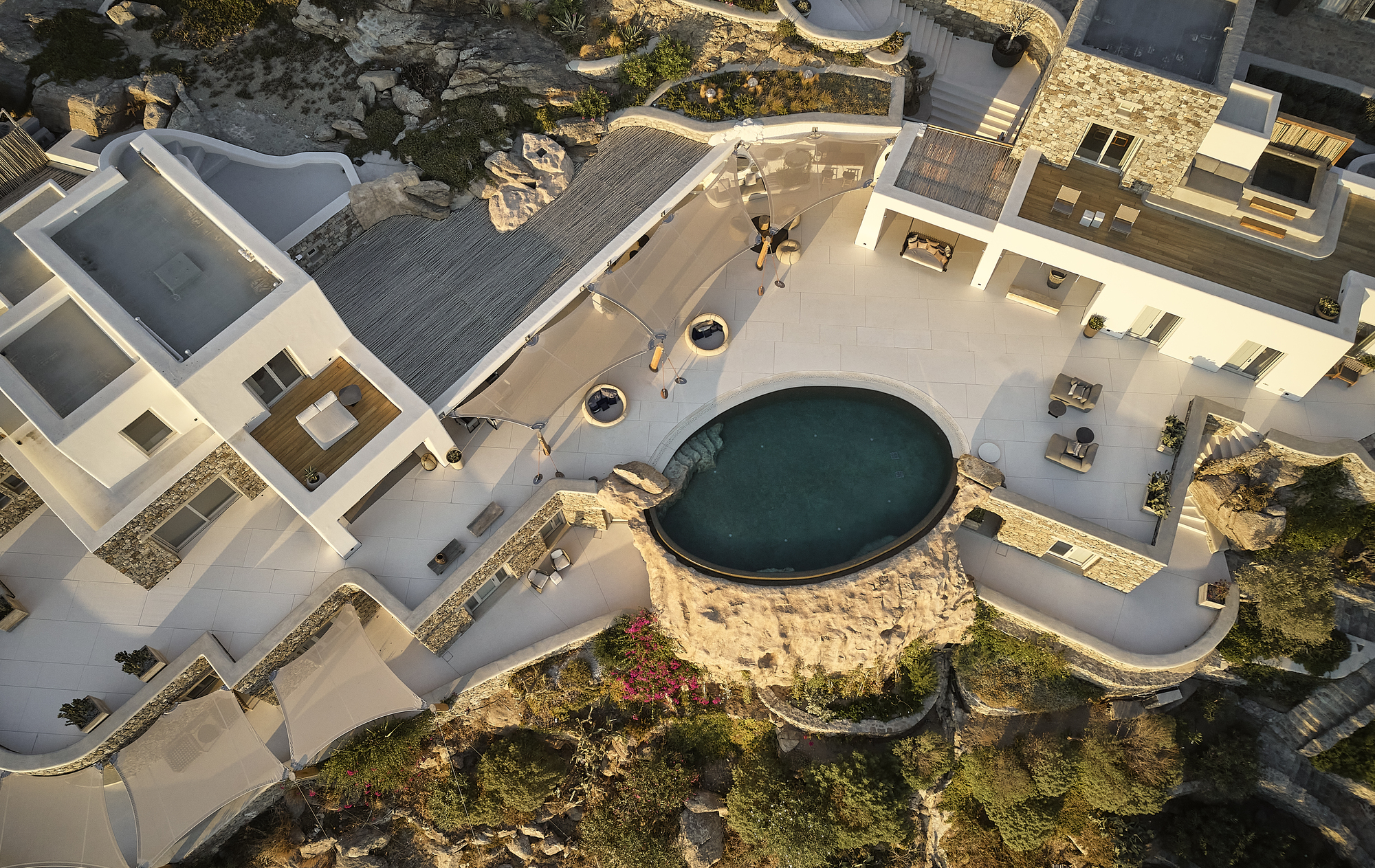 Aerial view of the white-rendered courtyards with circular pool integrated among natural rock outcroppings