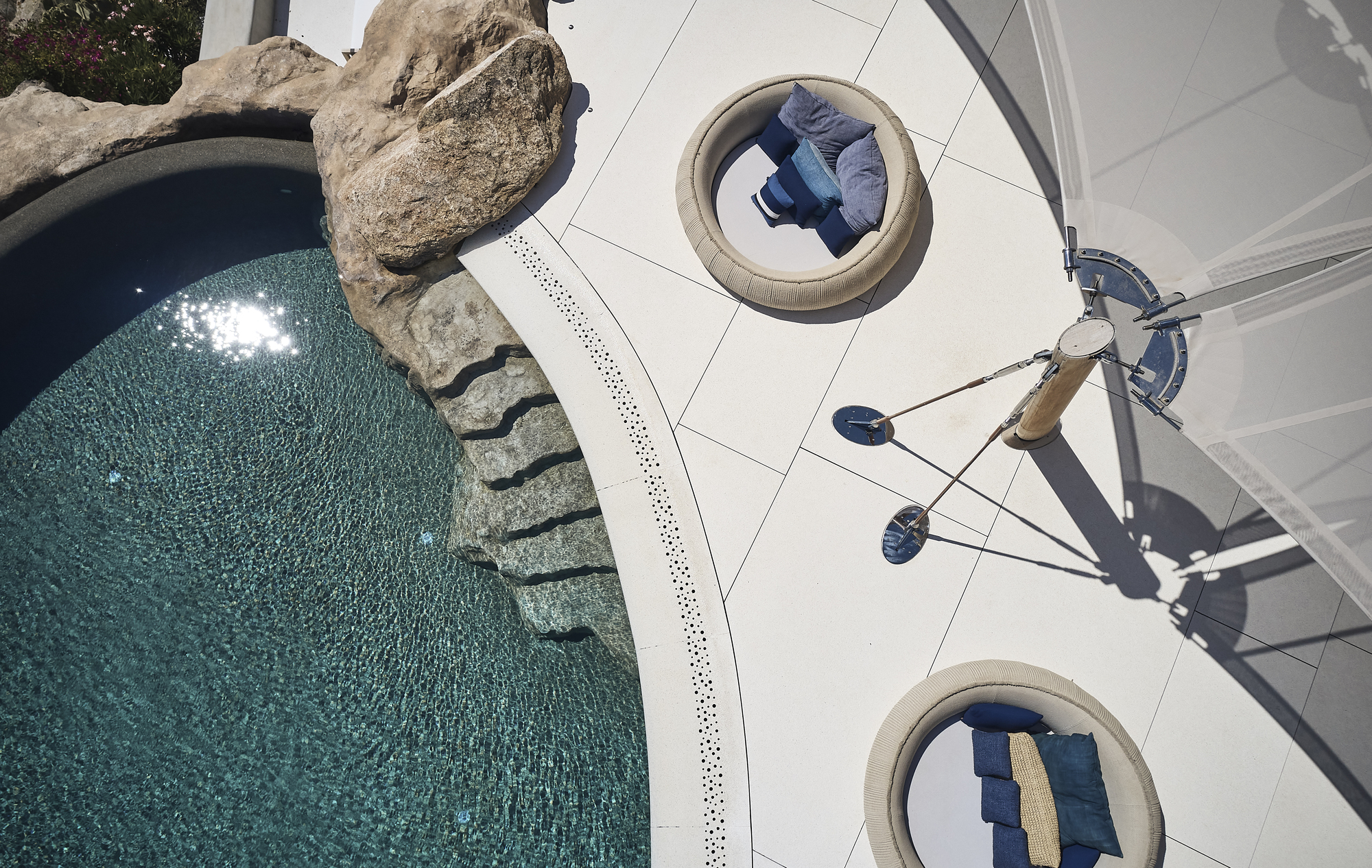 Overhead view of white terrace with circular recessed lounges and person walking beside the pool edge