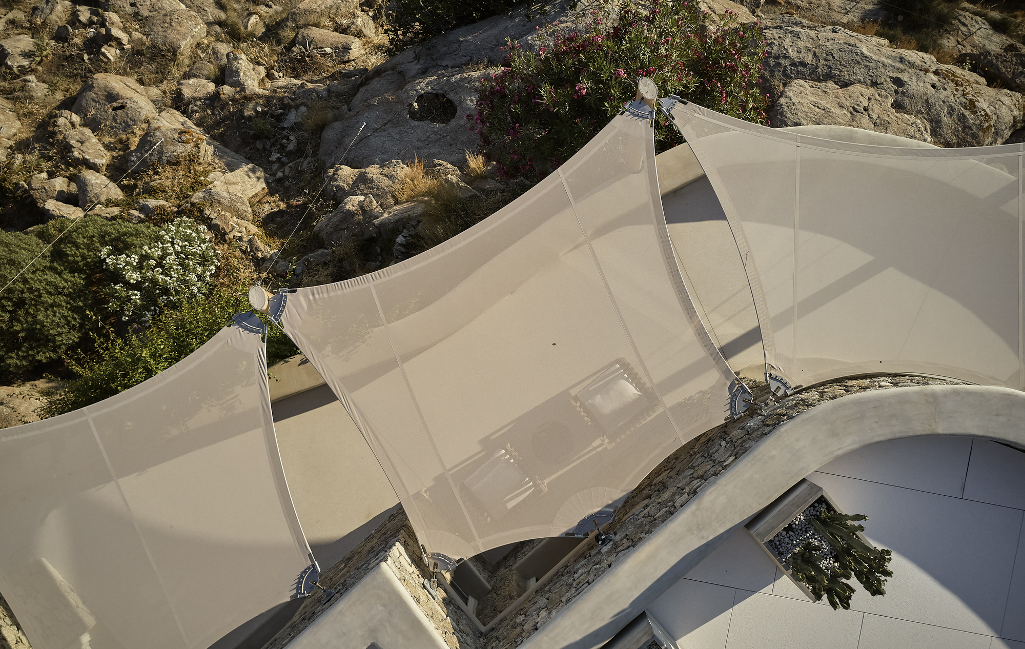 Angled view of the billowing tensile fabric canopy anchored between rocky terrain and white pavement