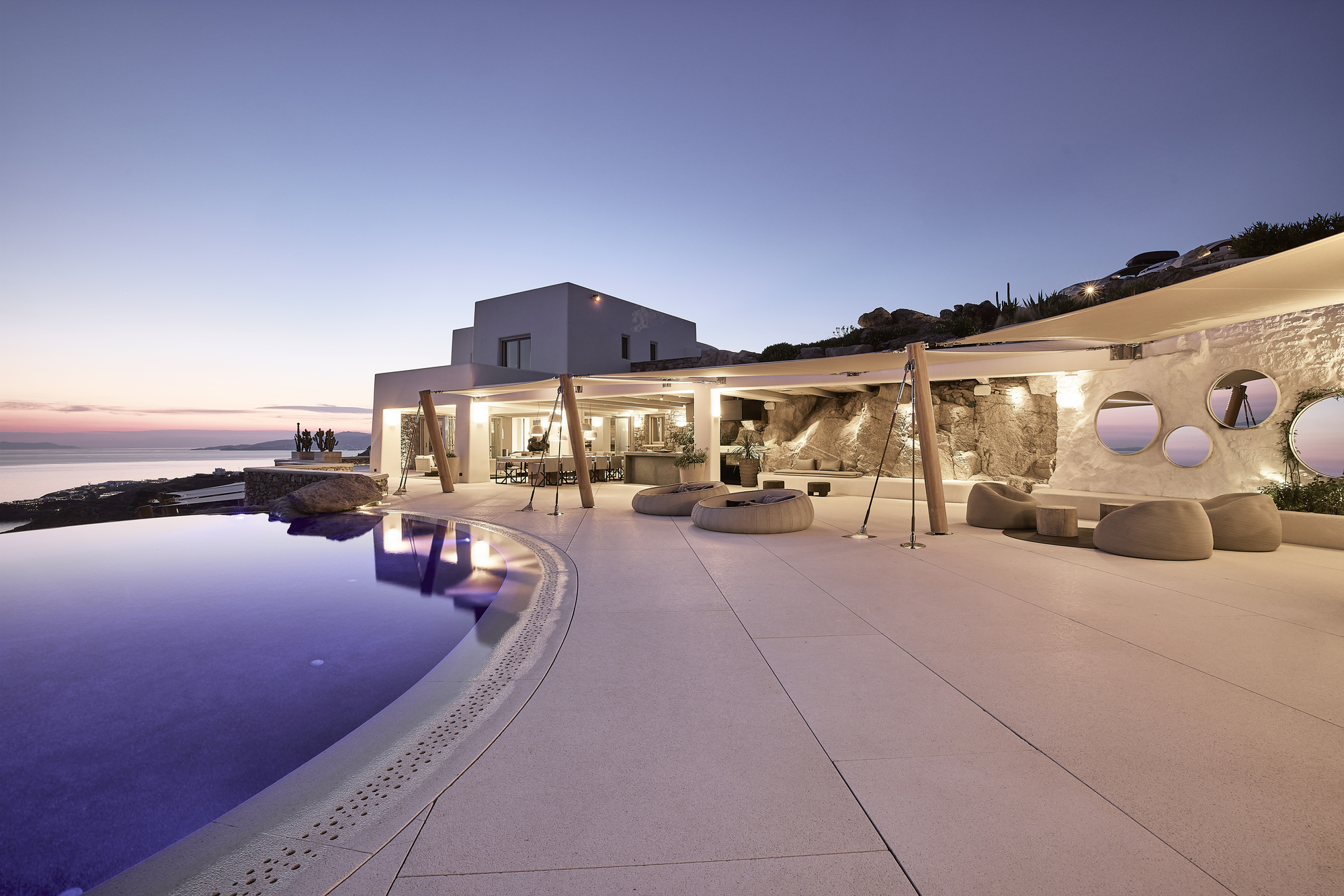 Infinity pool terrace with timber pergola and stone retaining wall at dusk overlooking the sea