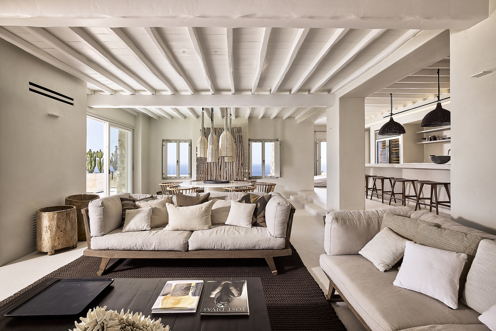 Open plan living space with white painted timber beams and ocean views through multiple openings