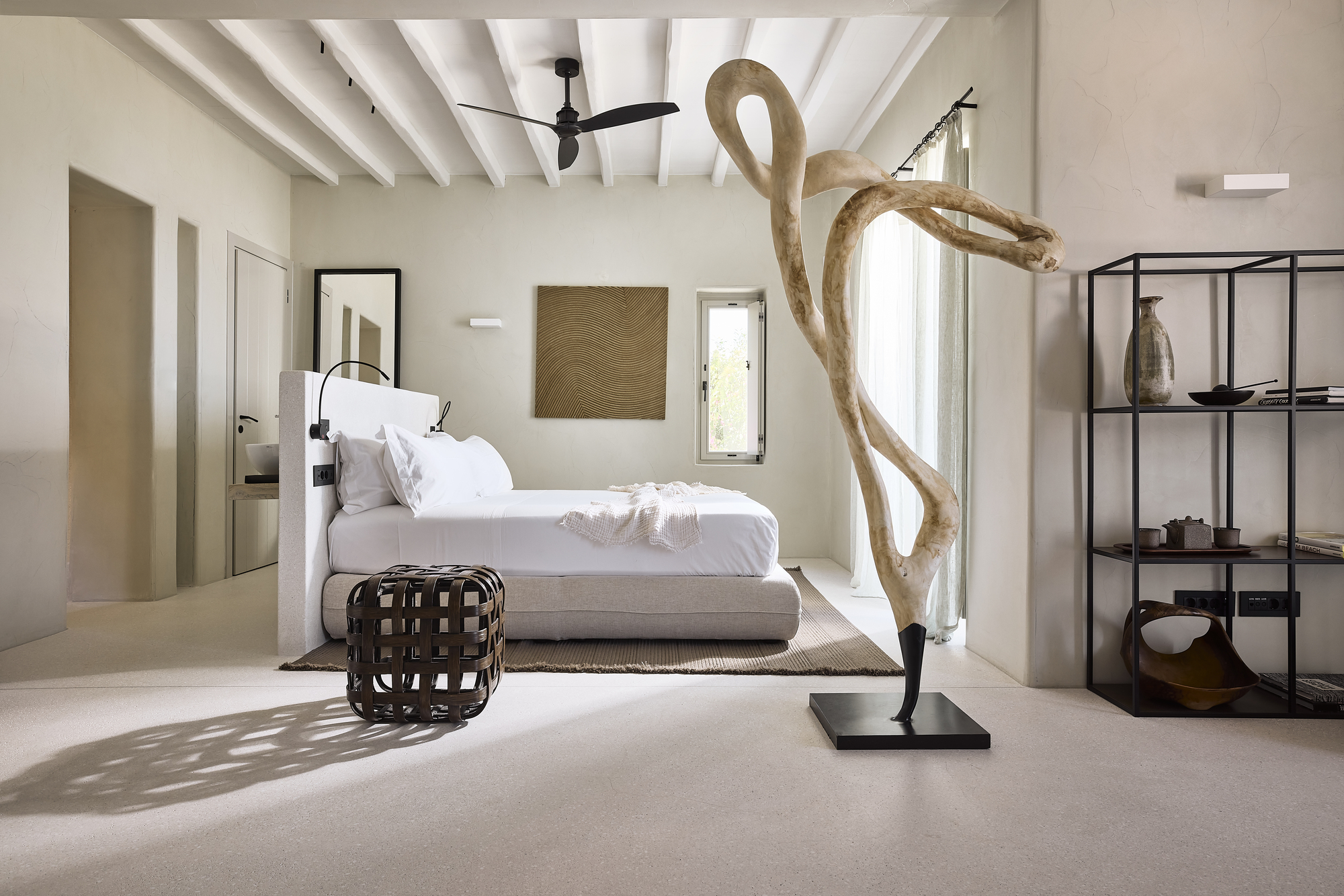Bedroom with exposed white timber ceiling beams and driftwood sculpture illuminated by afternoon sunlight