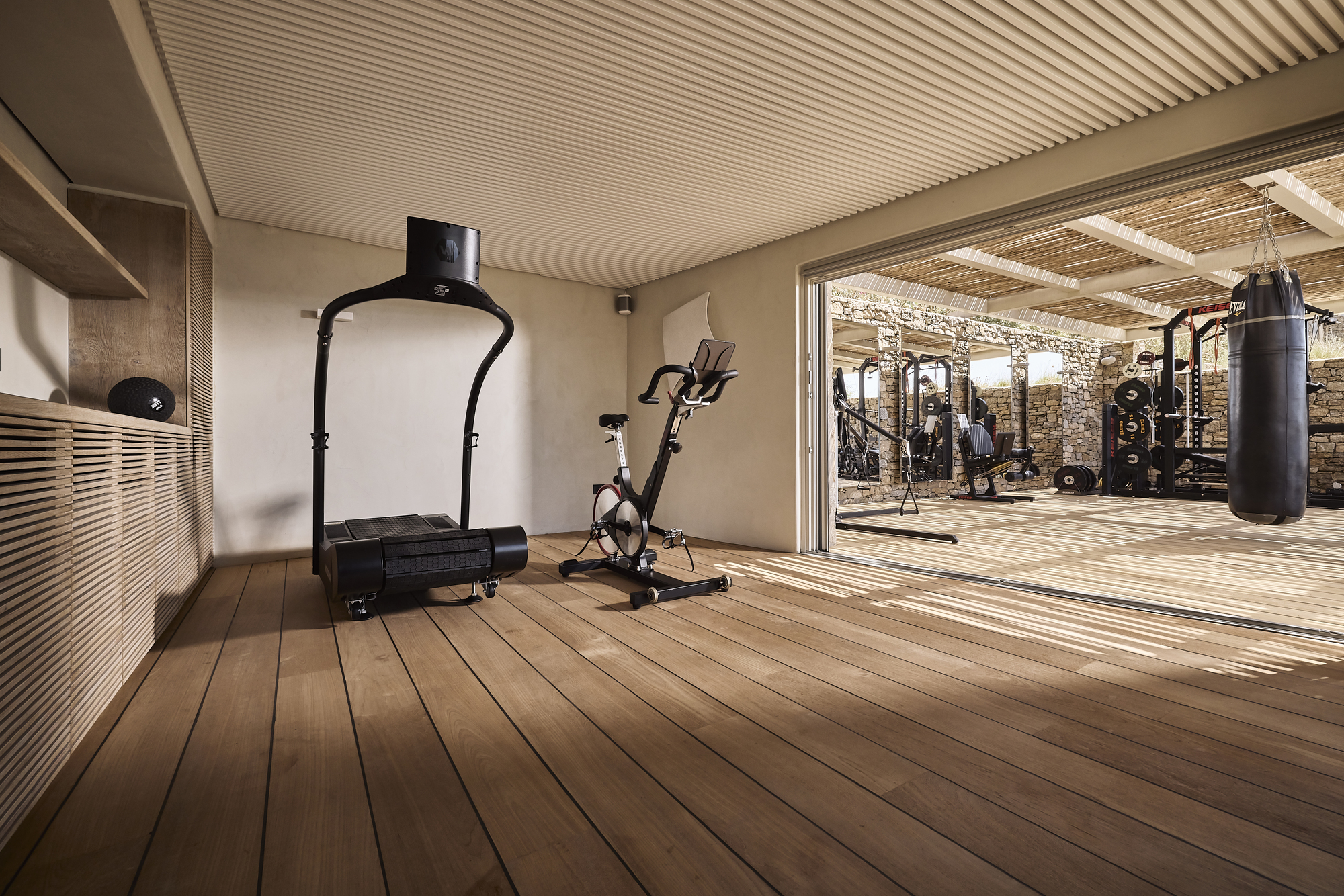 Interior fitness room with slatted timber ceiling and decking opening to an outdoor exercise area with stone walls