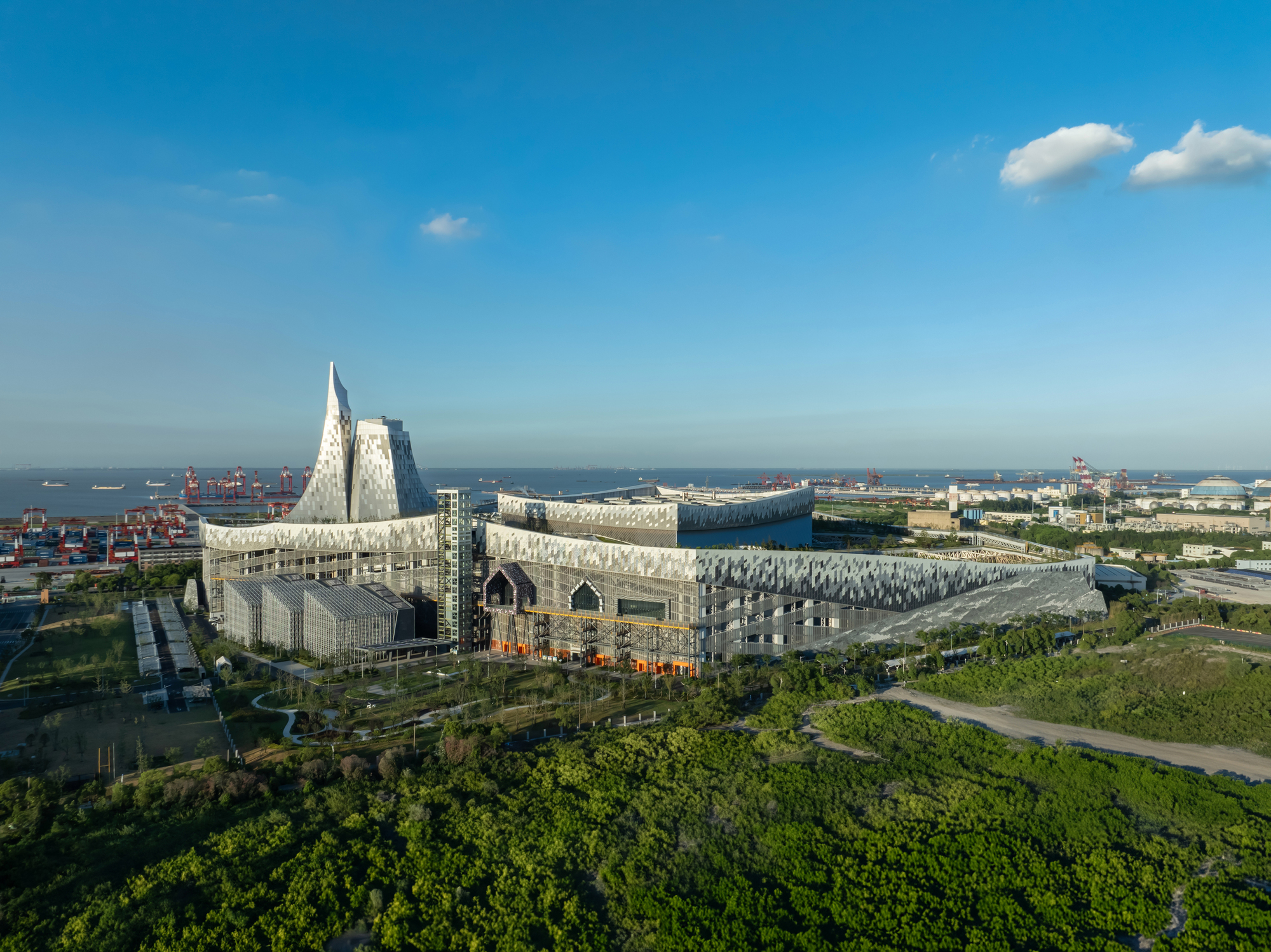 Aerial view of the perforated white metal facade complex surrounded by parkland and container port infrastructure