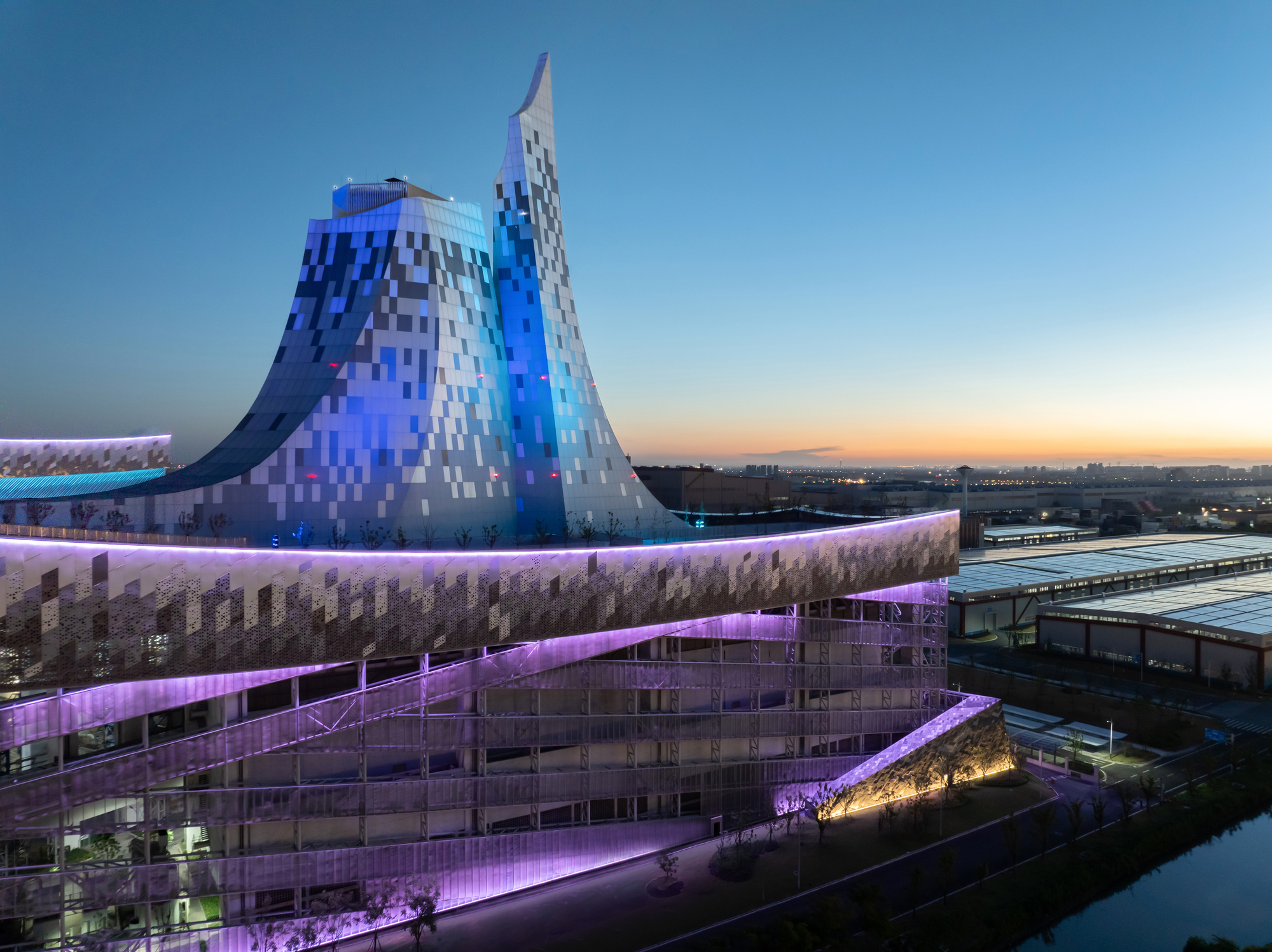 The pixelated tower with blue lighting rising above the terraced volumes at twilight