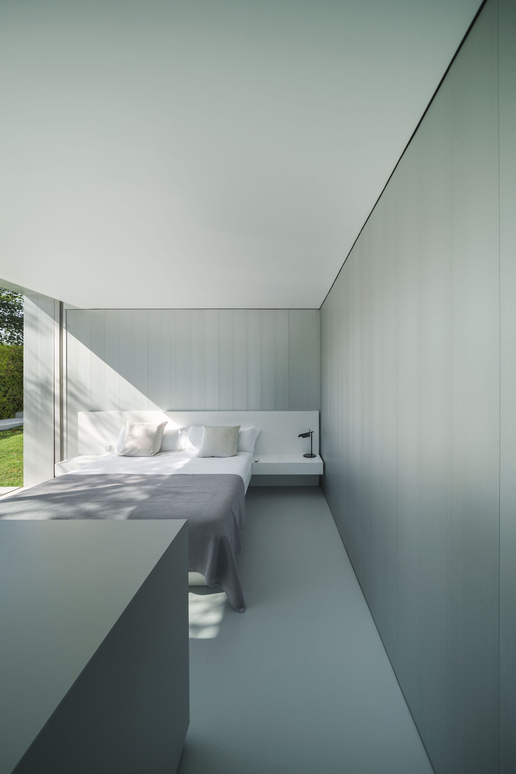 Bedroom with white built-in cabinetry and platform bed in afternoon sunlight from glass wall