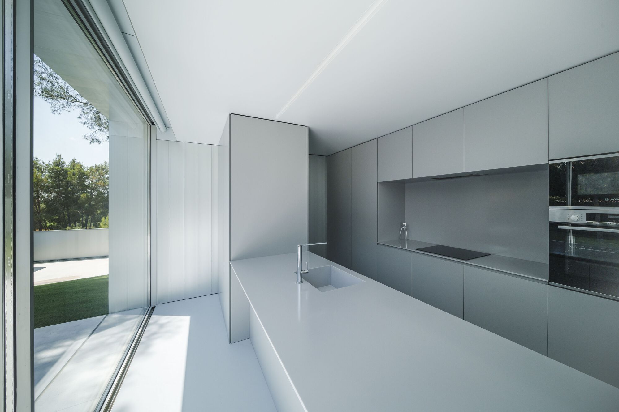 Kitchen with grey wall cabinetry and white island beneath recessed linear ceiling slot casting daylight