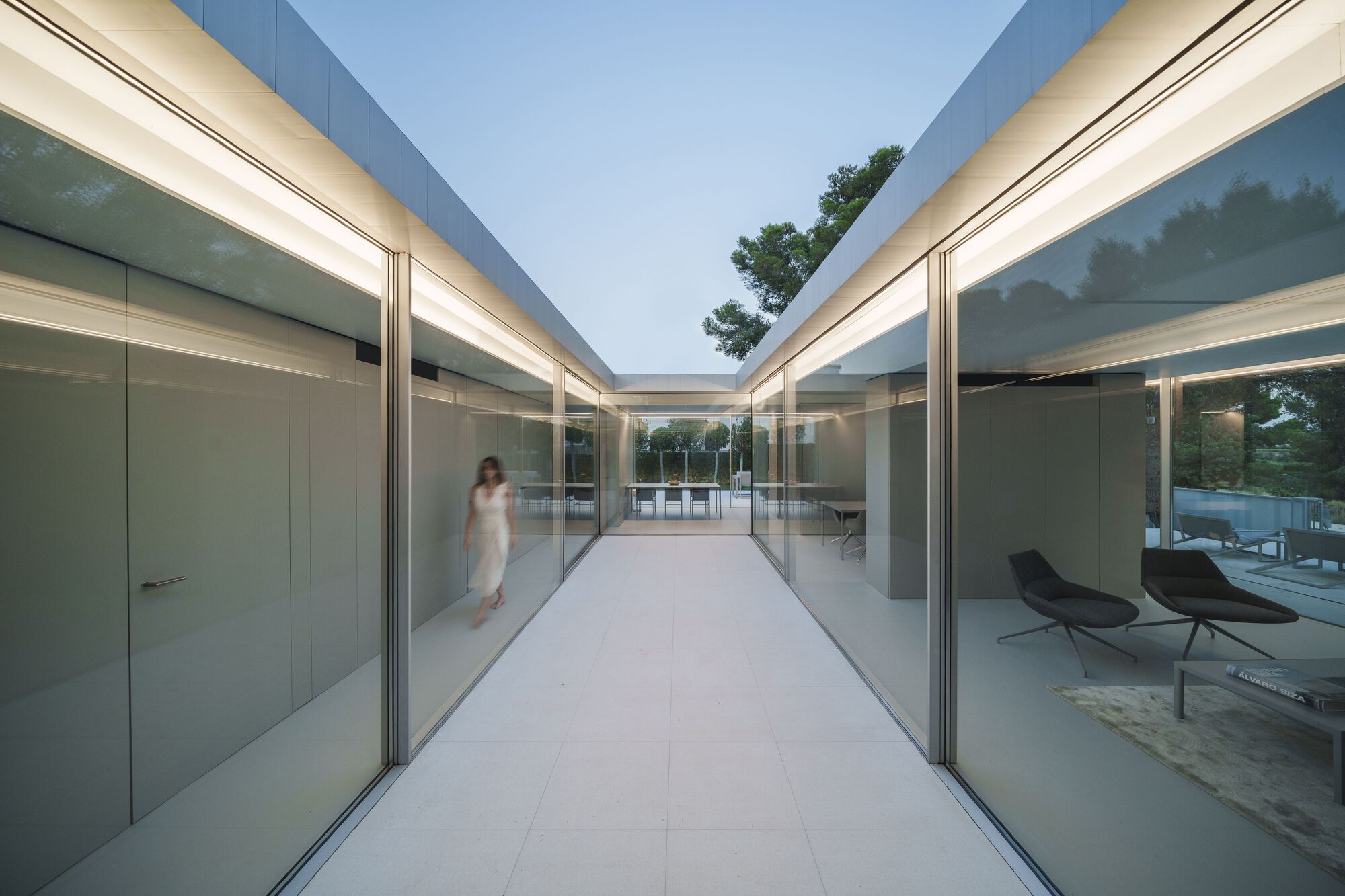 Glass corridor connecting two pavilions with a figure walking through at twilight