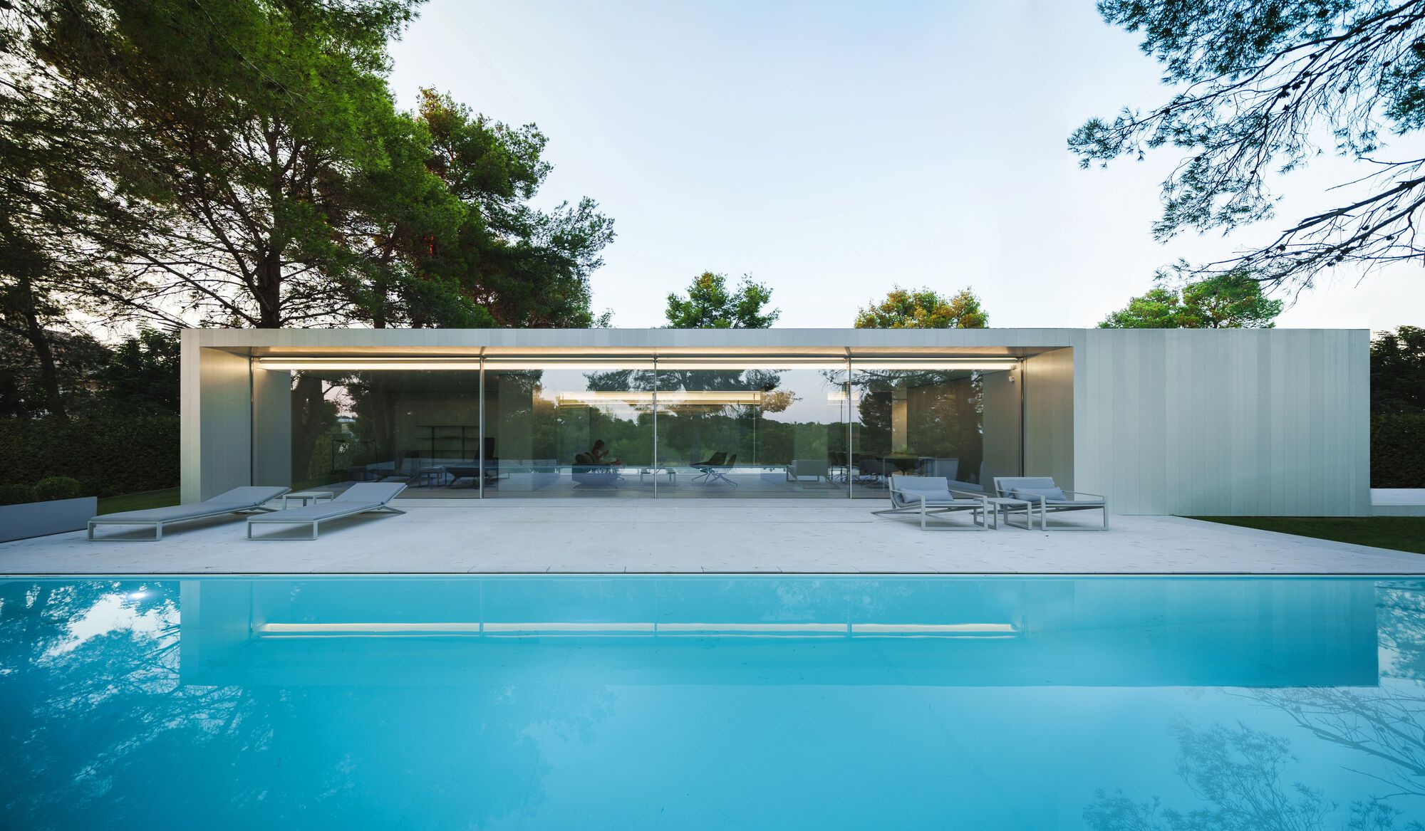 Swimming pool with cantilevered deck facing glass pavilion and surrounding pine trees
