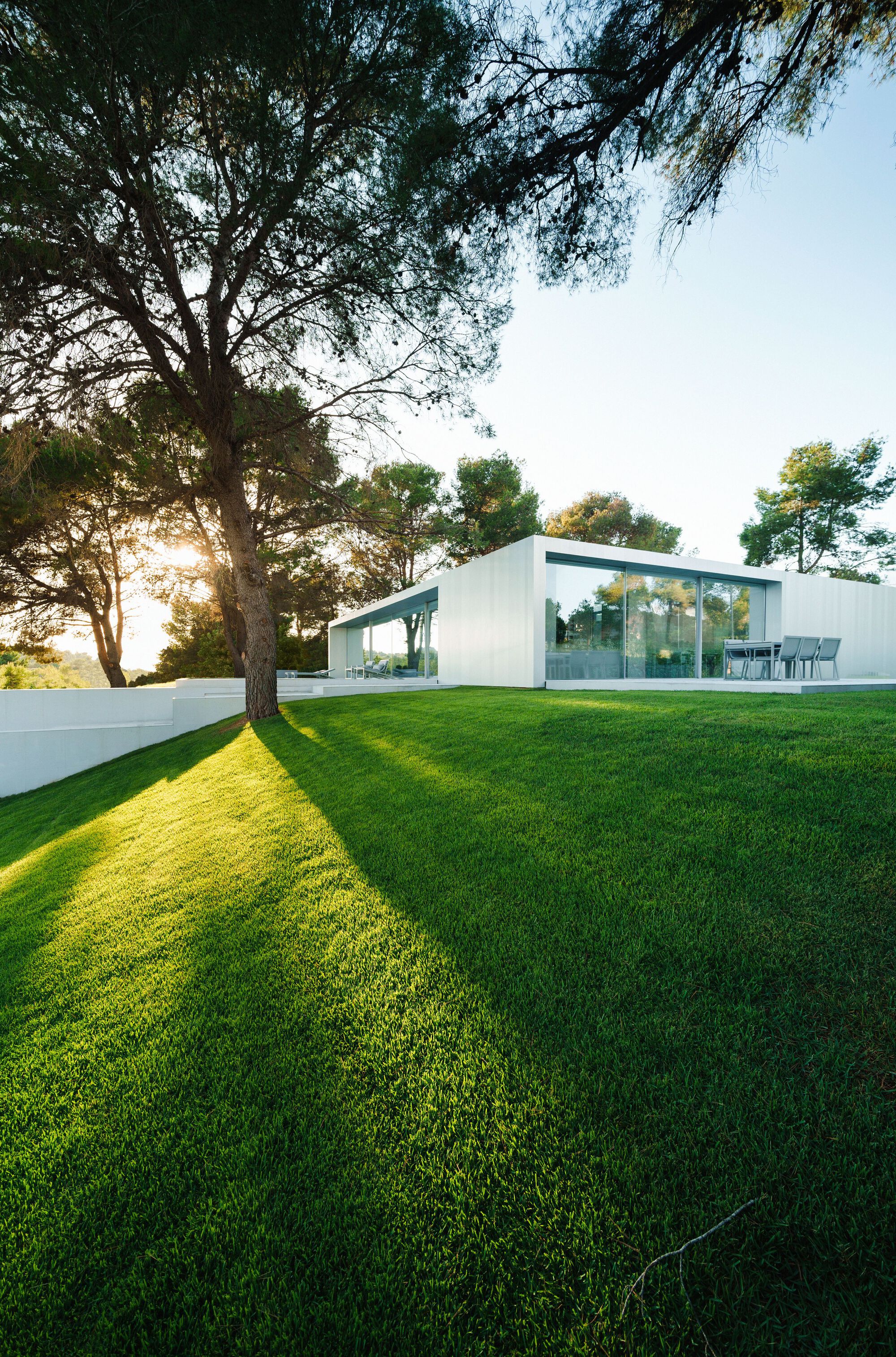 White single-story pavilion on mowed lawn with mature trees in late afternoon light
