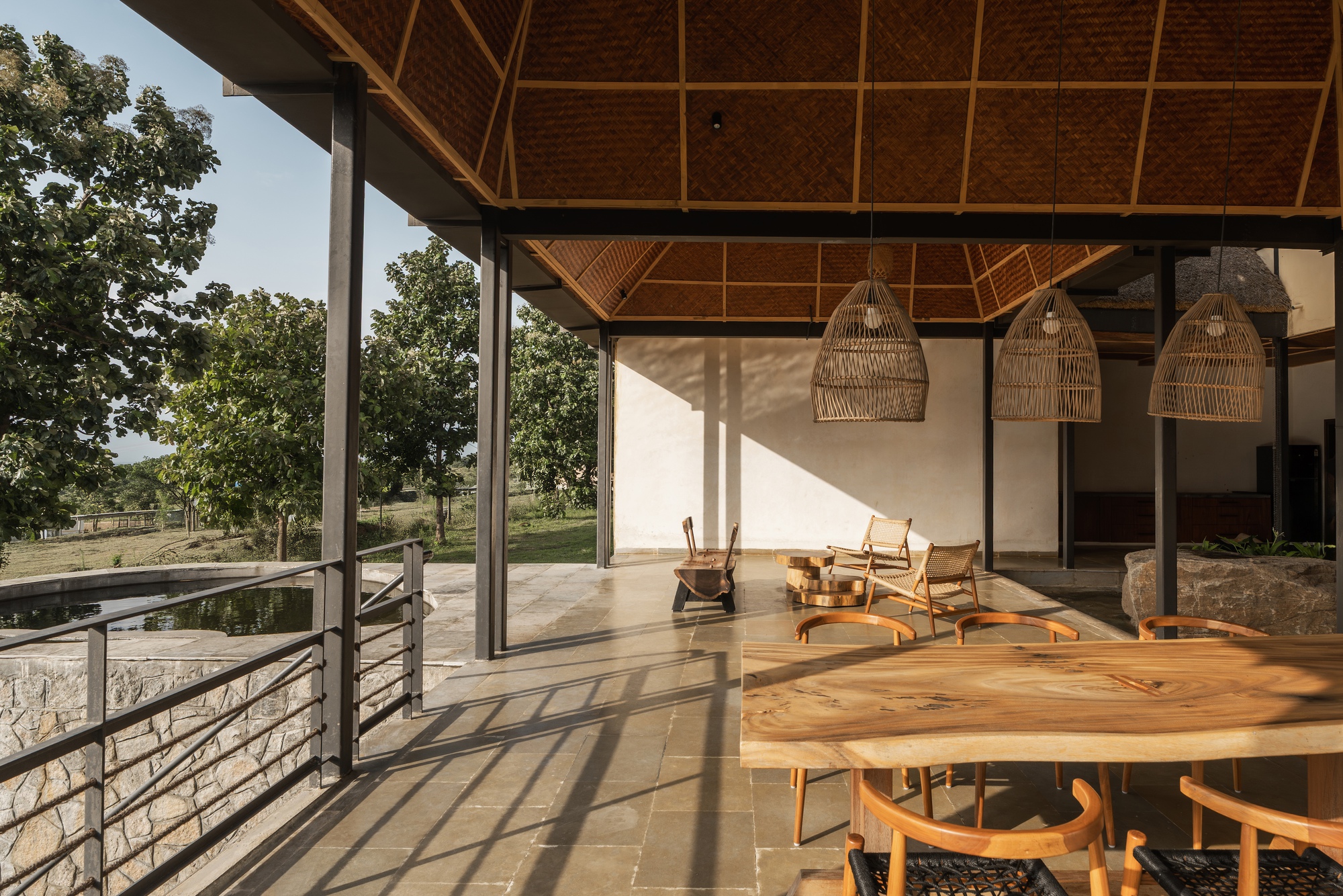 Covered terrace with diagonal lattice timber ceiling, woven pendant lights and patterned shadows on stone floor