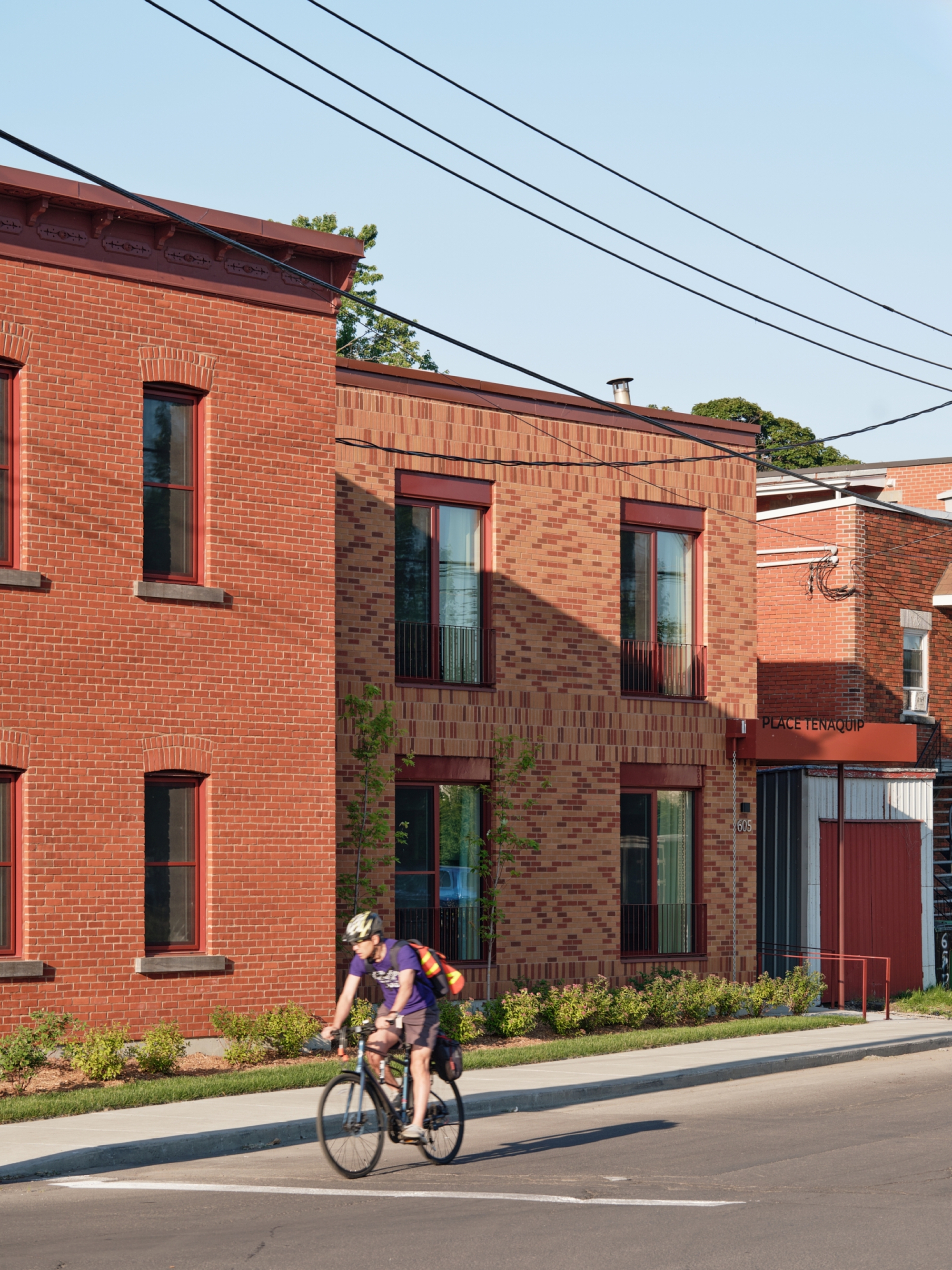 Street view of the brick facade with a cyclist passing the planted edge at ground level