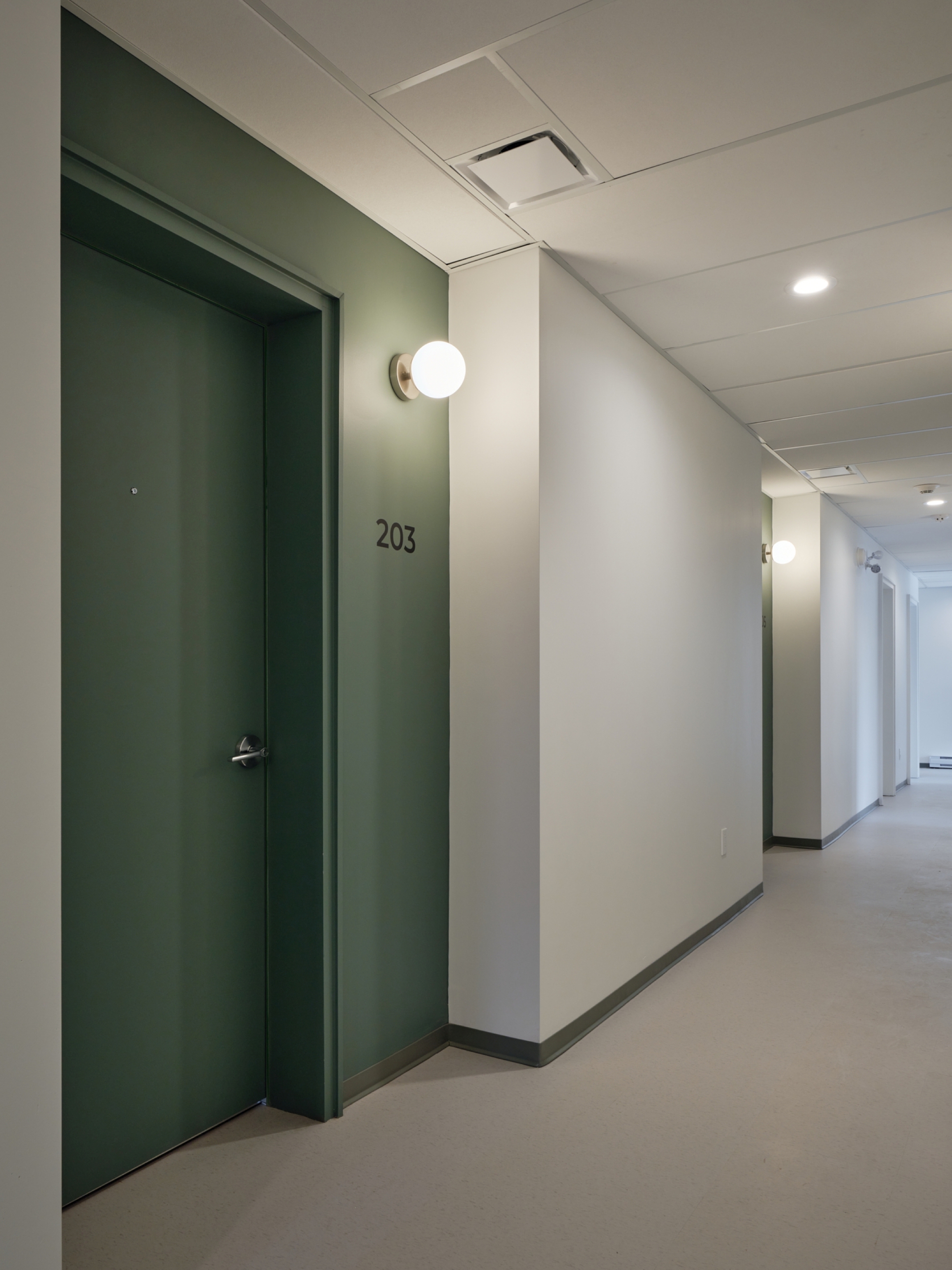Interior corridor with green painted door numbered 203 and white wall-mounted sphere light fixture