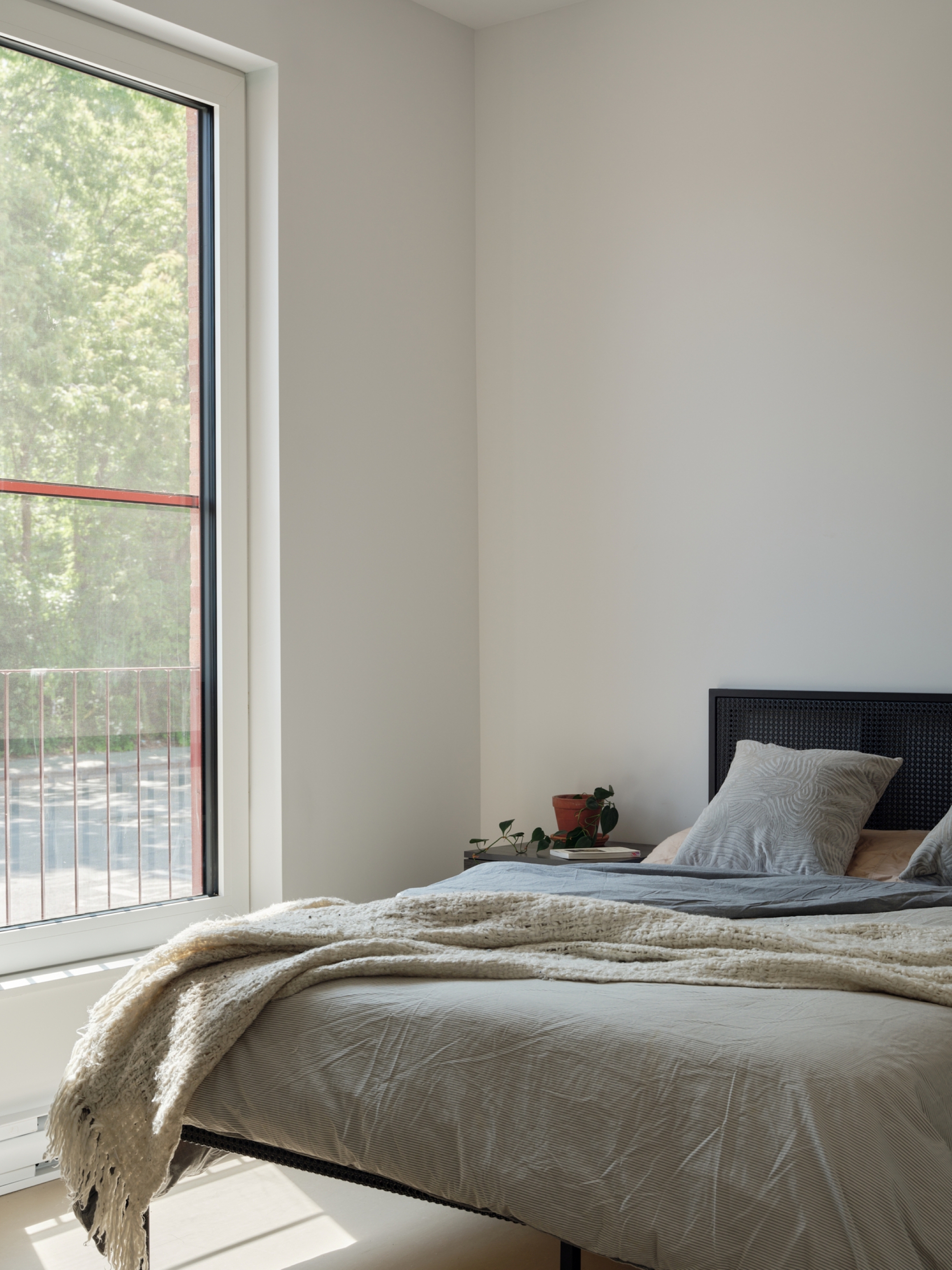 Bedroom with tall window overlooking balcony railings and trees in soft daylight