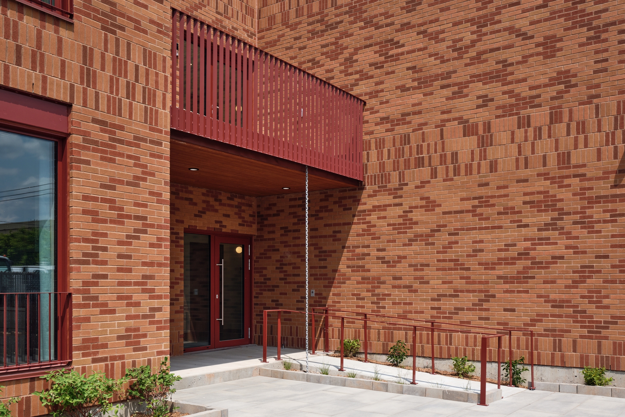 Recessed entrance courtyard with red metal screens and varied brick bond patterns on enclosing walls