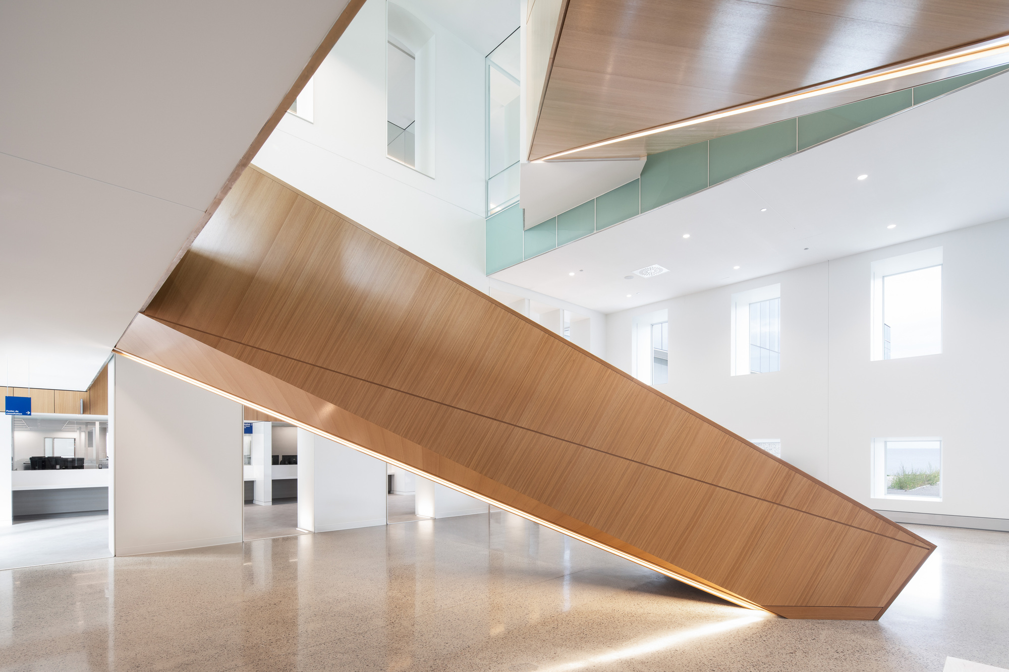 Tilted timber-clad staircase with integrated lighting rising through a double-height lobby with terrazzo flooring