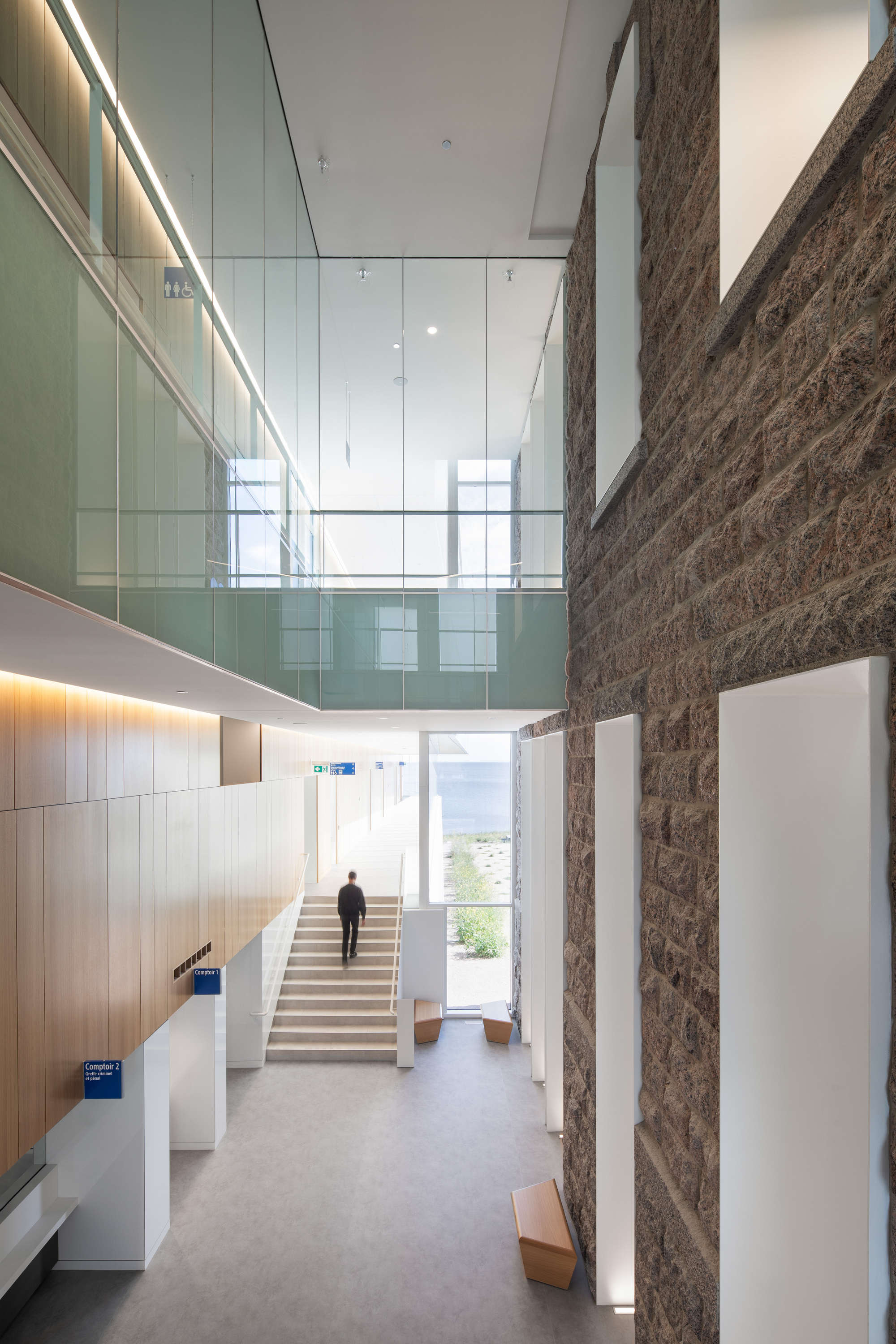 Multi-story atrium with glass balustrade overlooking a stone entry stair where a person ascends