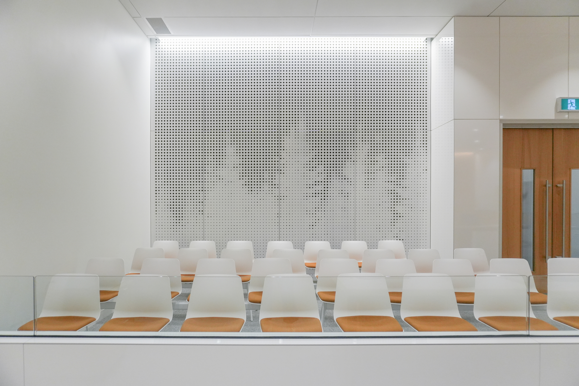 Gallery seating facing a perforated metal screen wall with illuminated borders and wood elevator doors