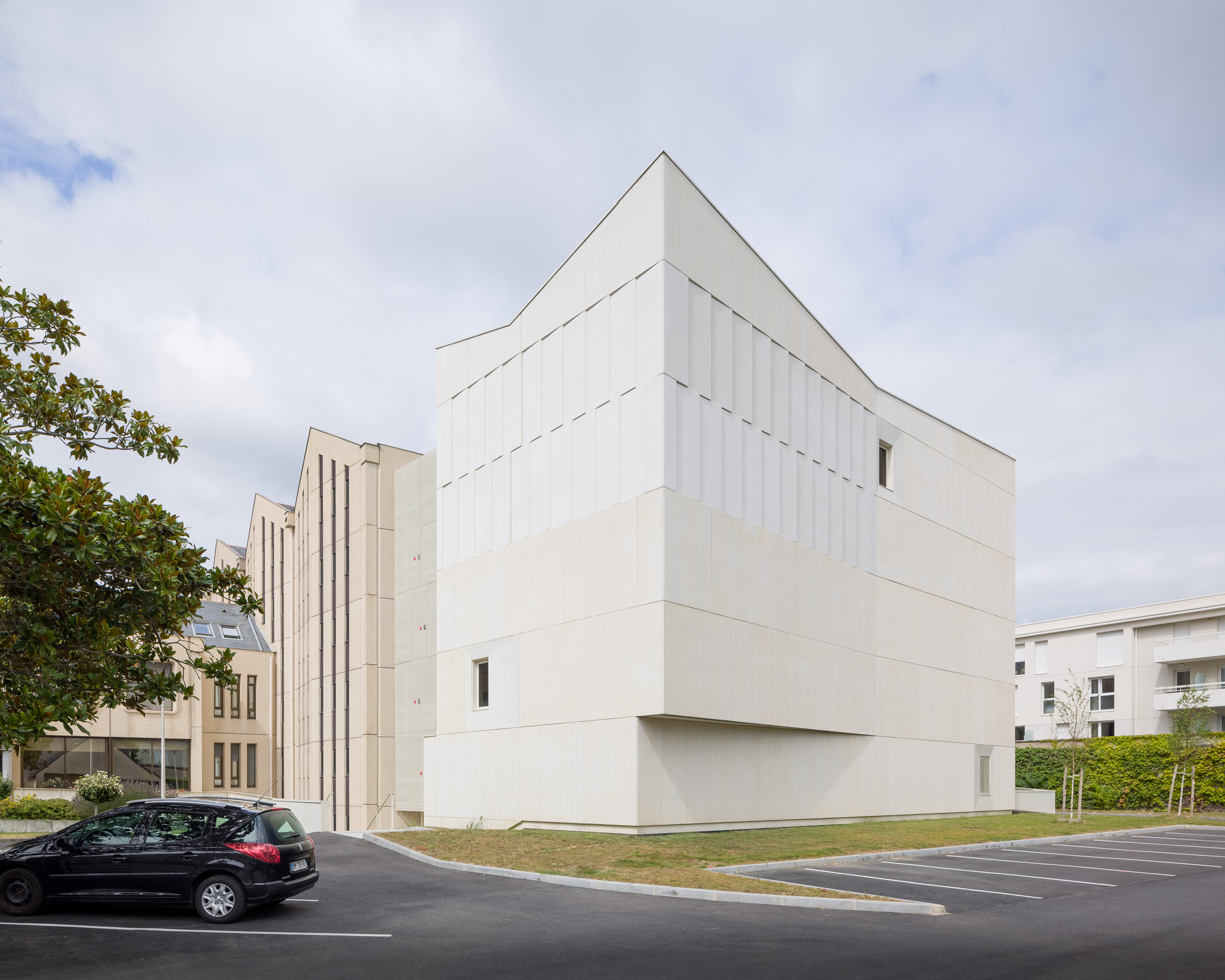 Corner view of the gabled volume with vertical panel cladding under overcast skies with parked car