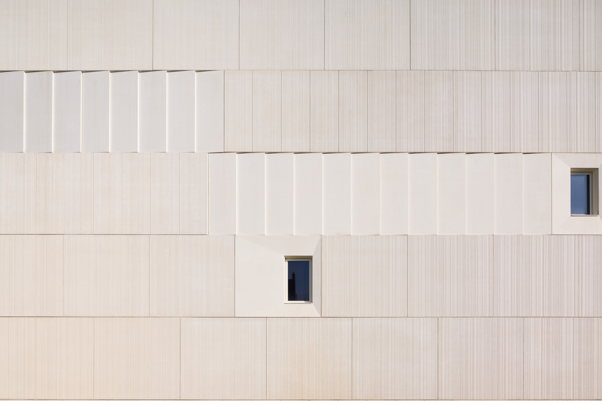 Facade detail showing vertically striated panels with offset joints and two small rectangular window openings