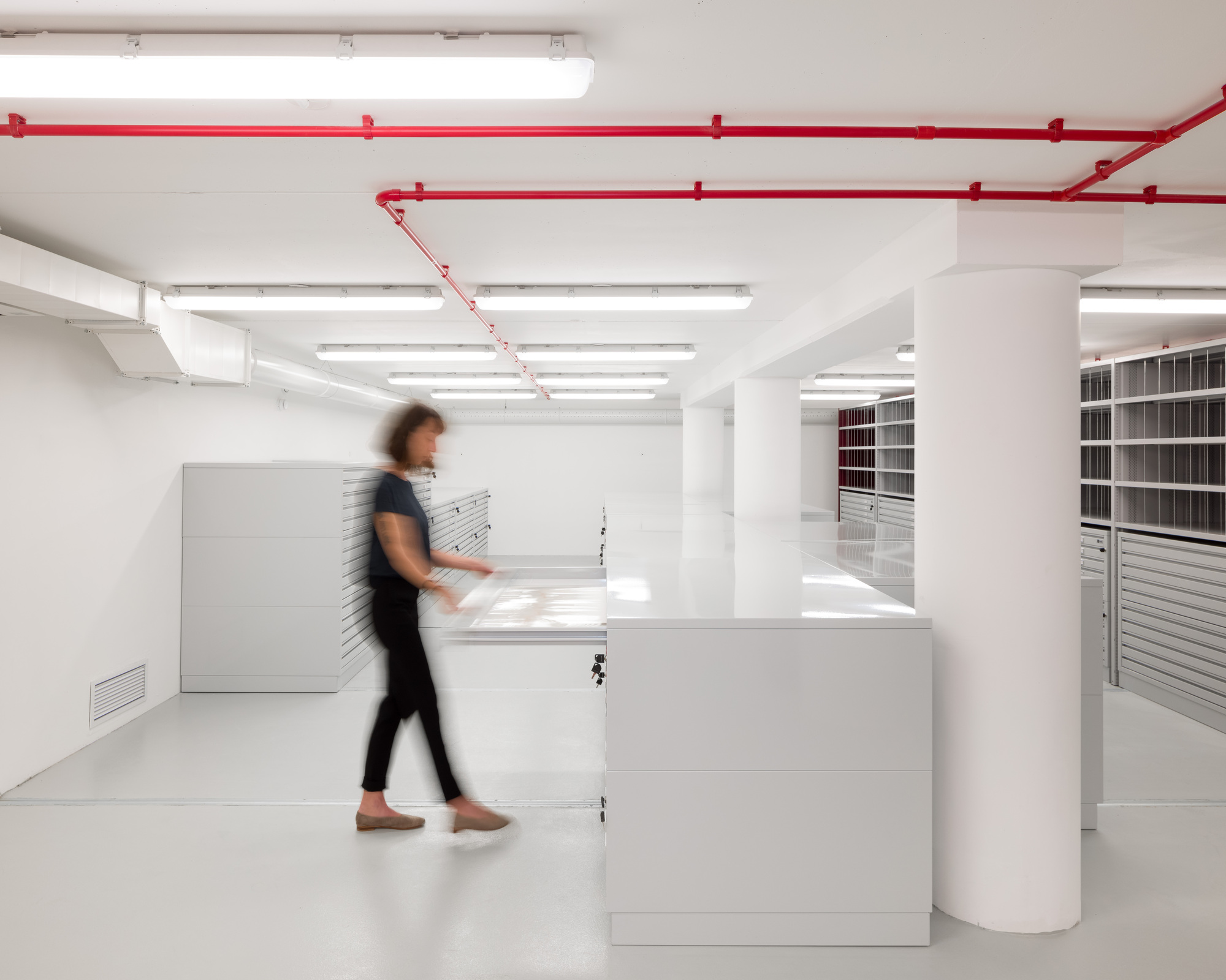 White reception desk with blurred figure walking past red exposed conduit on ceiling