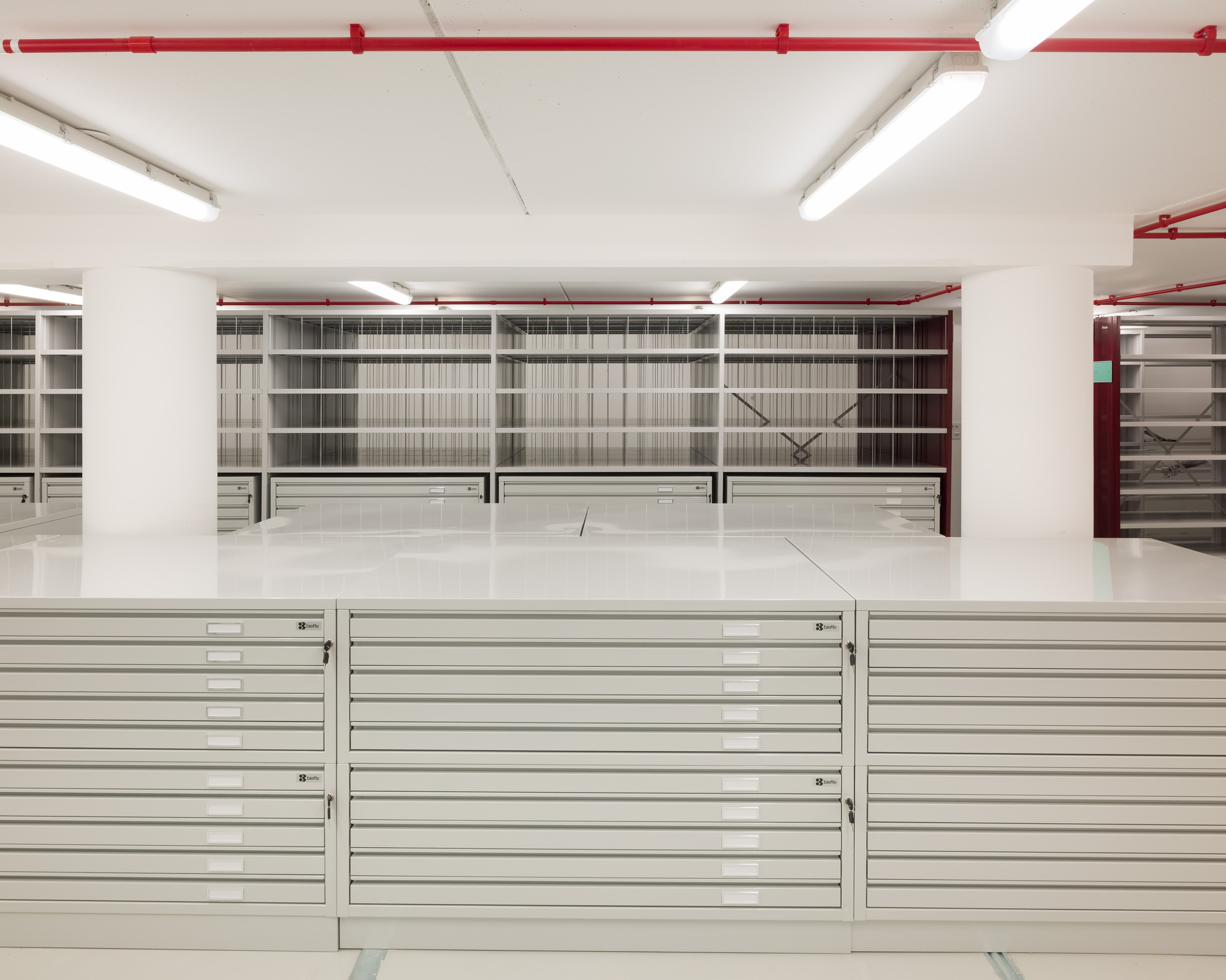 Flat file storage cabinets below wall-mounted shelving units in a white-walled archive space