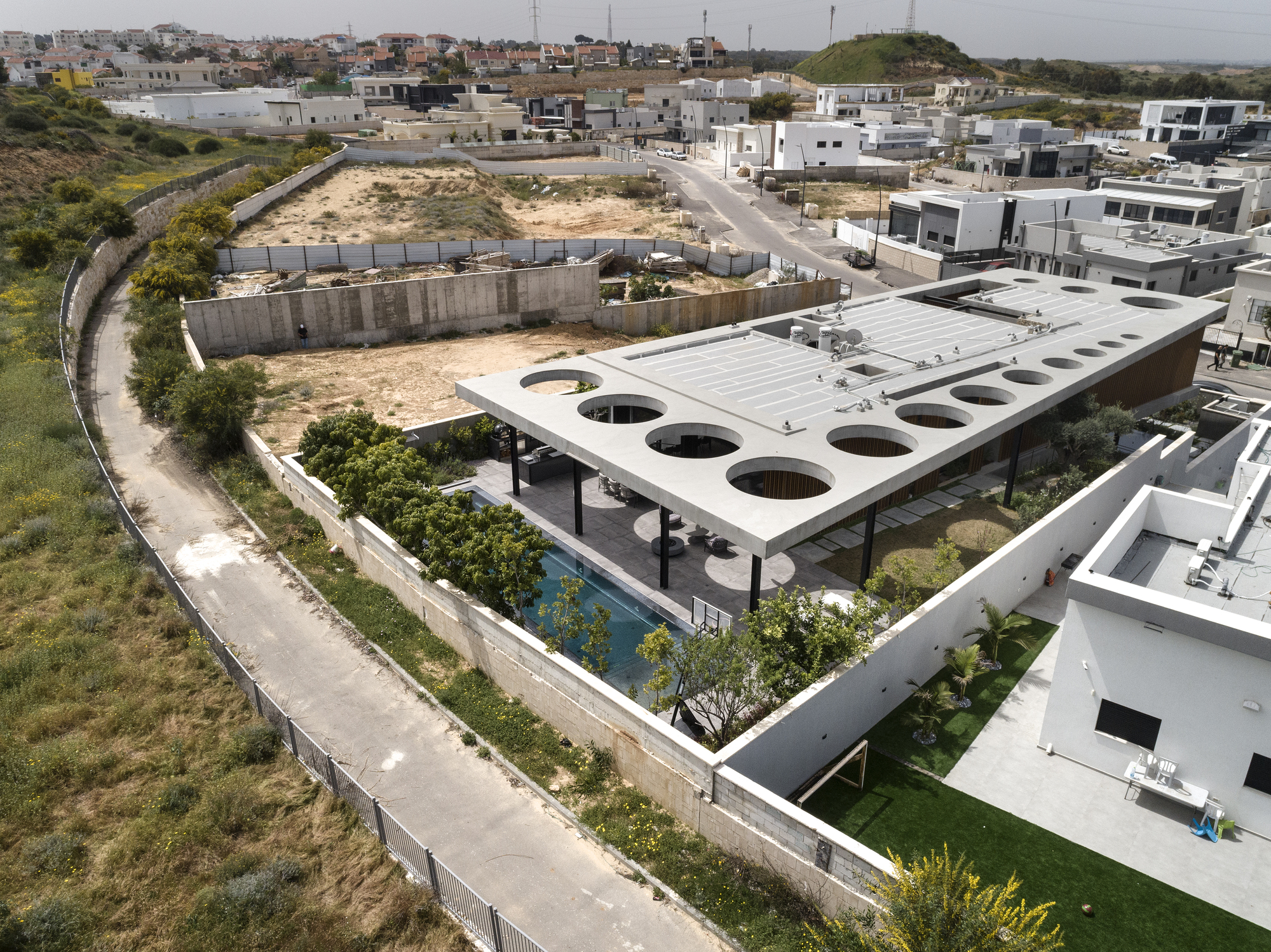 Aerial view of white concrete roof with circular voids over terraced gardens in hillside neighborhood