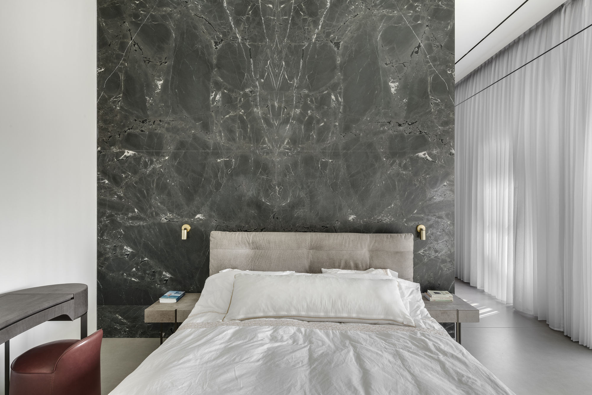 Bedroom with bookmatched grey marble headboard wall and sheer curtains filtering daylight