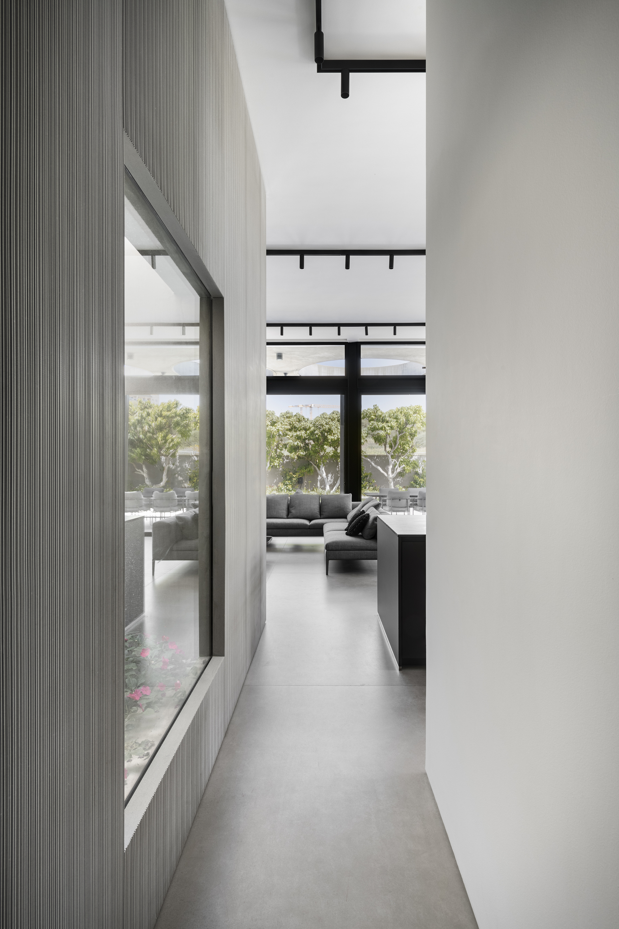 Narrow corridor with fluted grey wall panels and high clerestory windows overlooking a planted courtyard