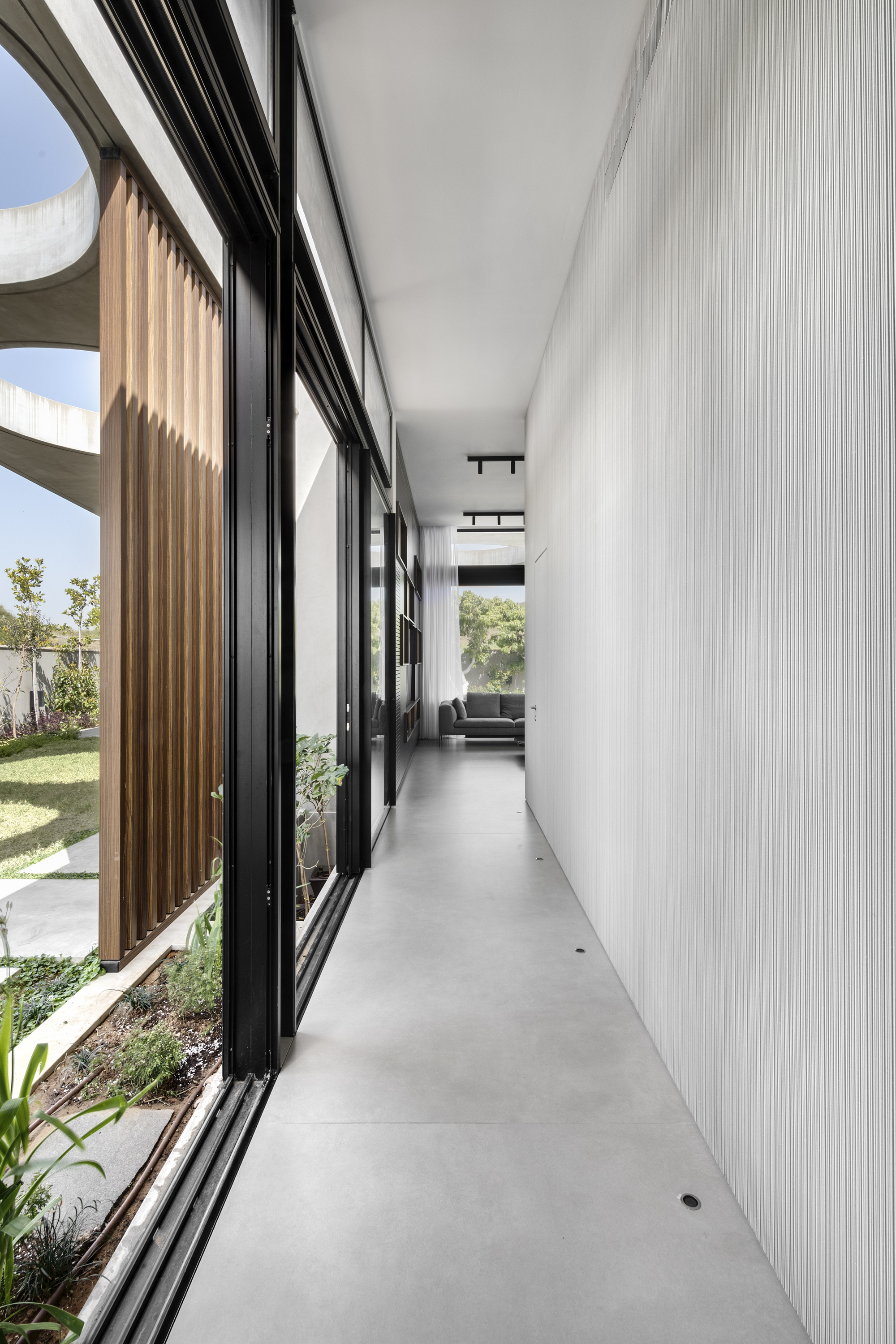 Interior hallway with black-framed glazing and timber vertical screens filtering afternoon sunlight