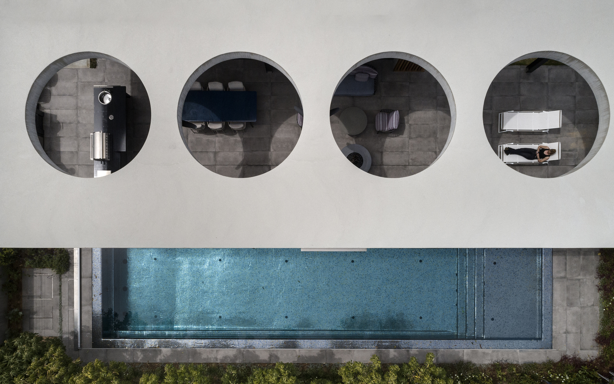 Overhead view of four circular openings in a white roof revealing interior spaces and a lap pool below