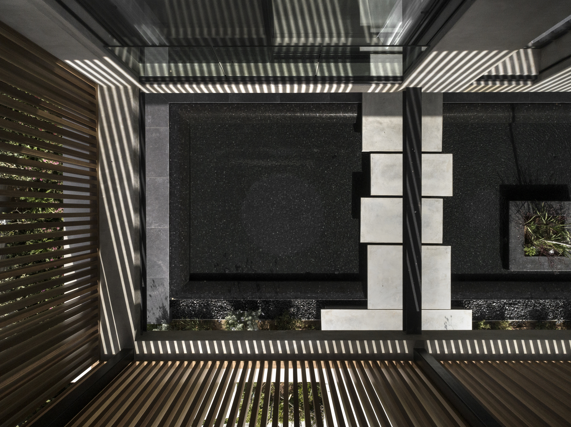 Looking up through a courtyard void showing horizontal slatted screens casting striped shadows across dark walls