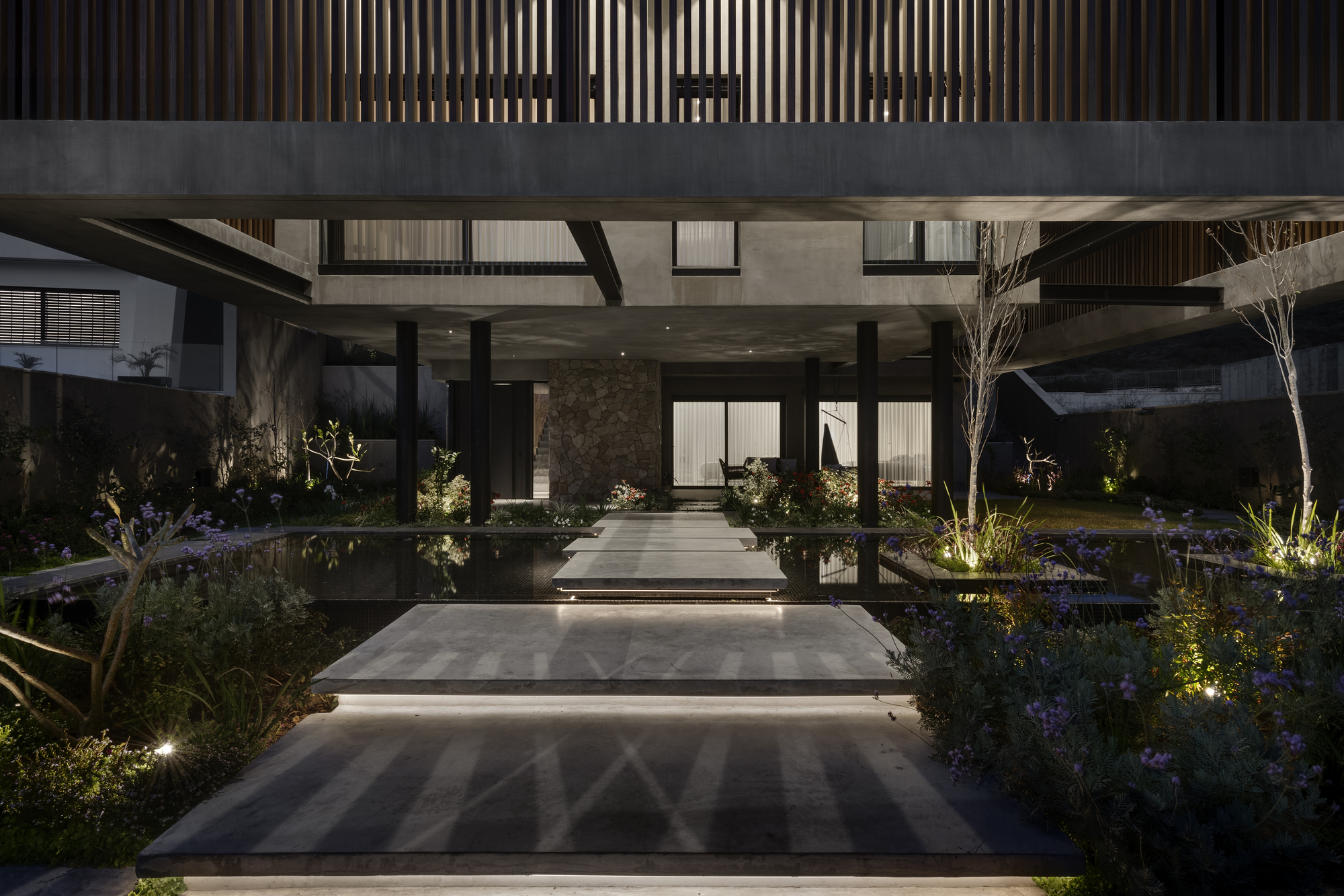 Illuminated entrance pathway with reflecting pools flanking concrete stepping stones at dusk