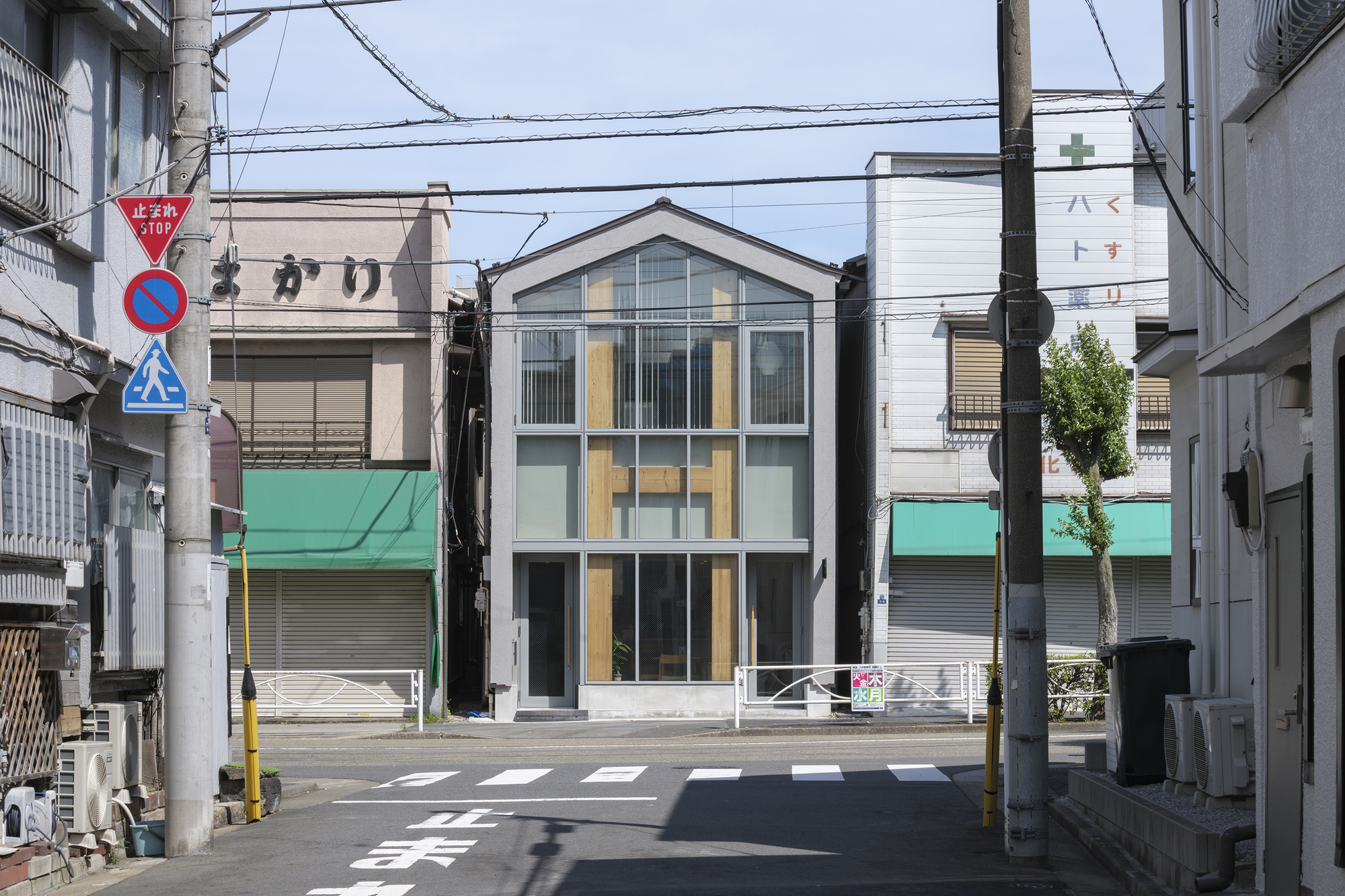 Street view of the three-storey gabled facade with timber-framed glazing beneath overhead power lines